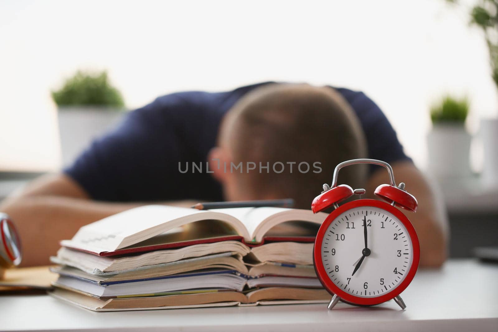 Close-up of tired student take nap behind pile of textbooks on table. Sleepy man resting during education after sleepless night. Despair, deadline concept