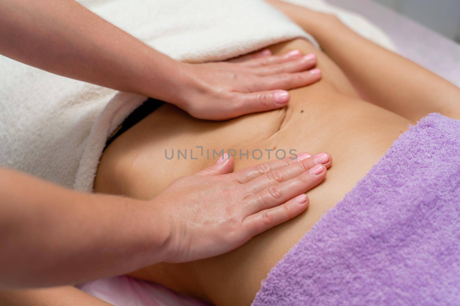 Top view of hands massaging female abdomen.Therapist applying pressure on belly. Woman receiving massage at spa salon by Matiunina