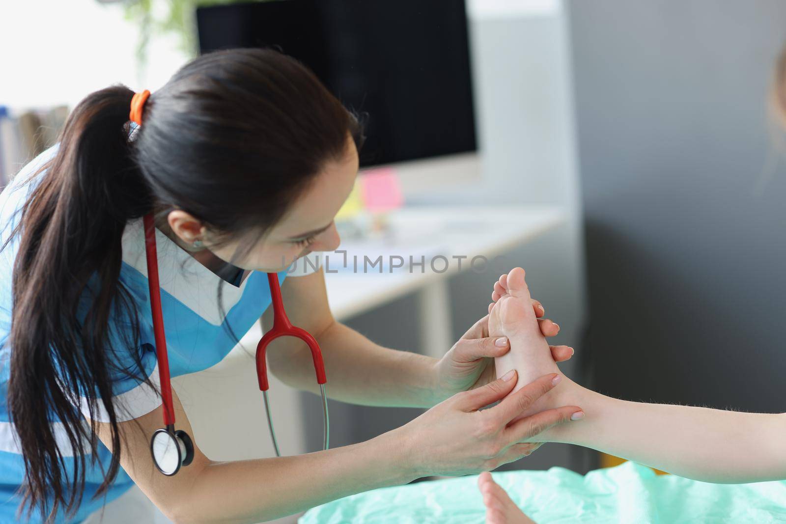 Portrait of trauma surgeon specialist examine child foot on planned appointment in clinic. Woman doctor in uniform look at foot. Health, diagnostic concept