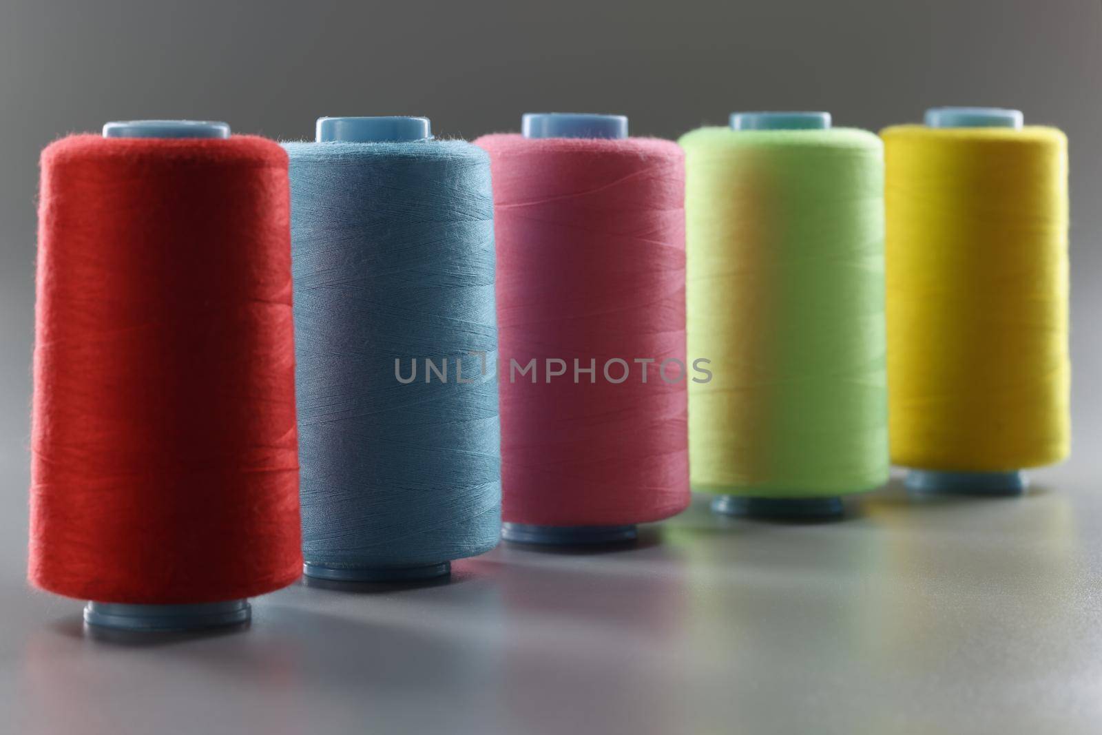 Close-up of group of whole haberdashery item colorful thread spools on grey surface. Colorful bobbins for tailoring. Dressmaking, atelier, fashion concept