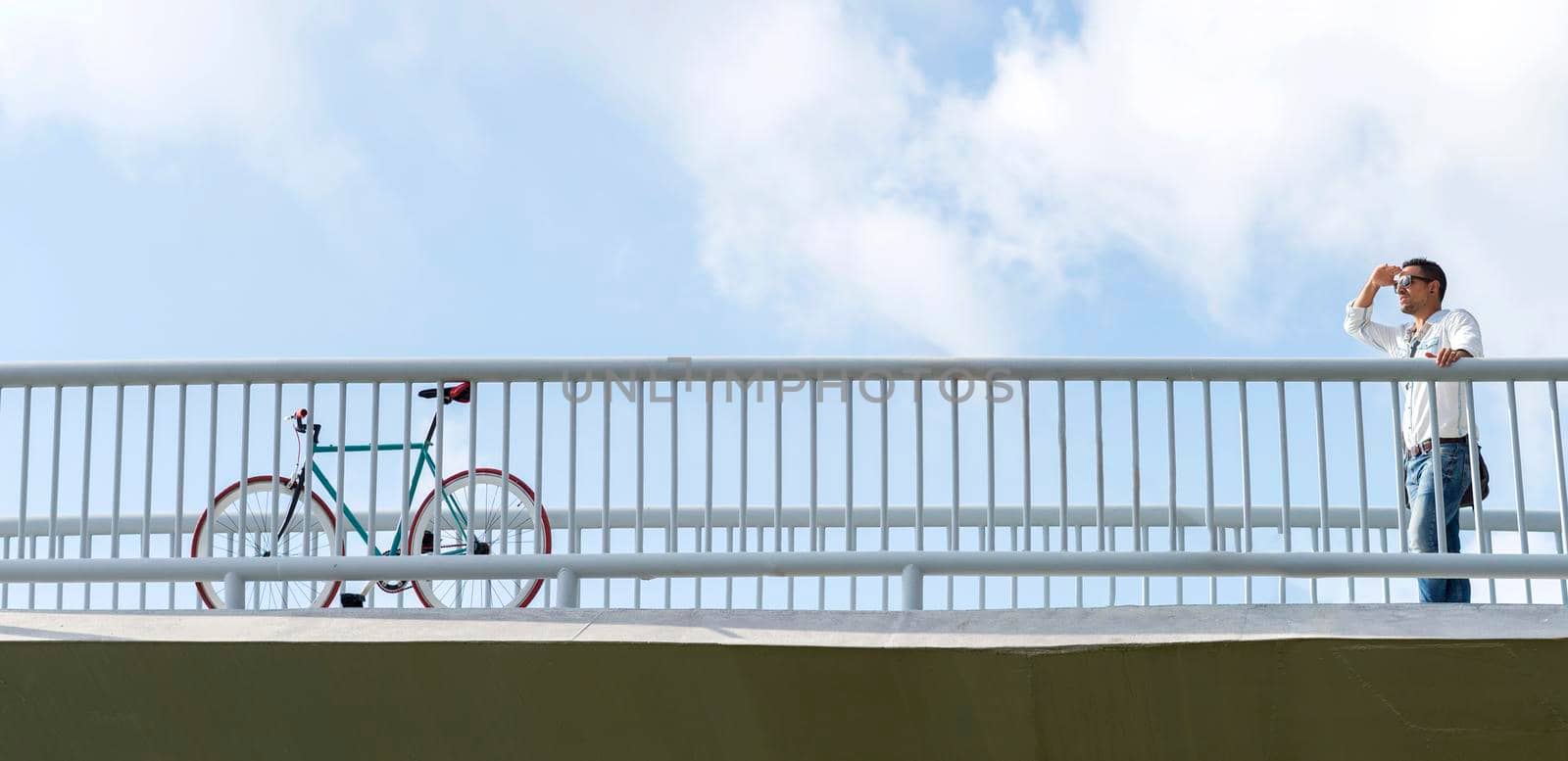 Young business man with sunglasses looking far away to a vintage bike on a bridge by raferto1973