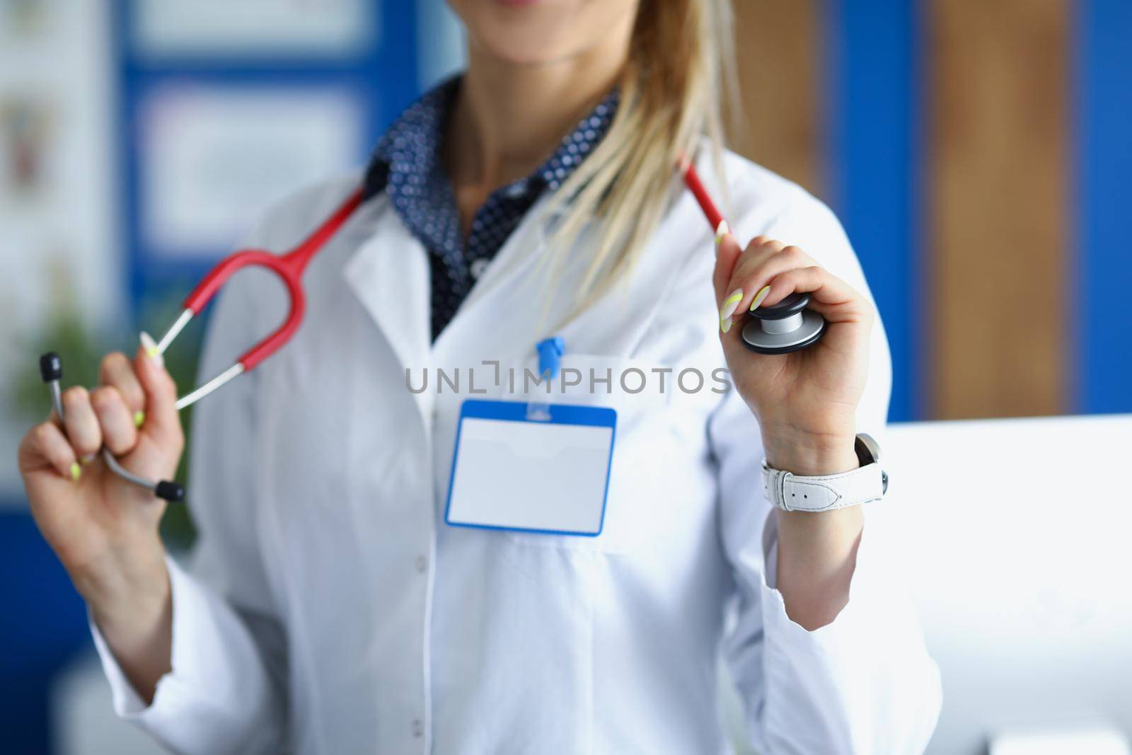 Close-up of female medical worker in white uniform posing with stethoscope on neck. Young woman specialist in office. Healthcare, appointment, help concept