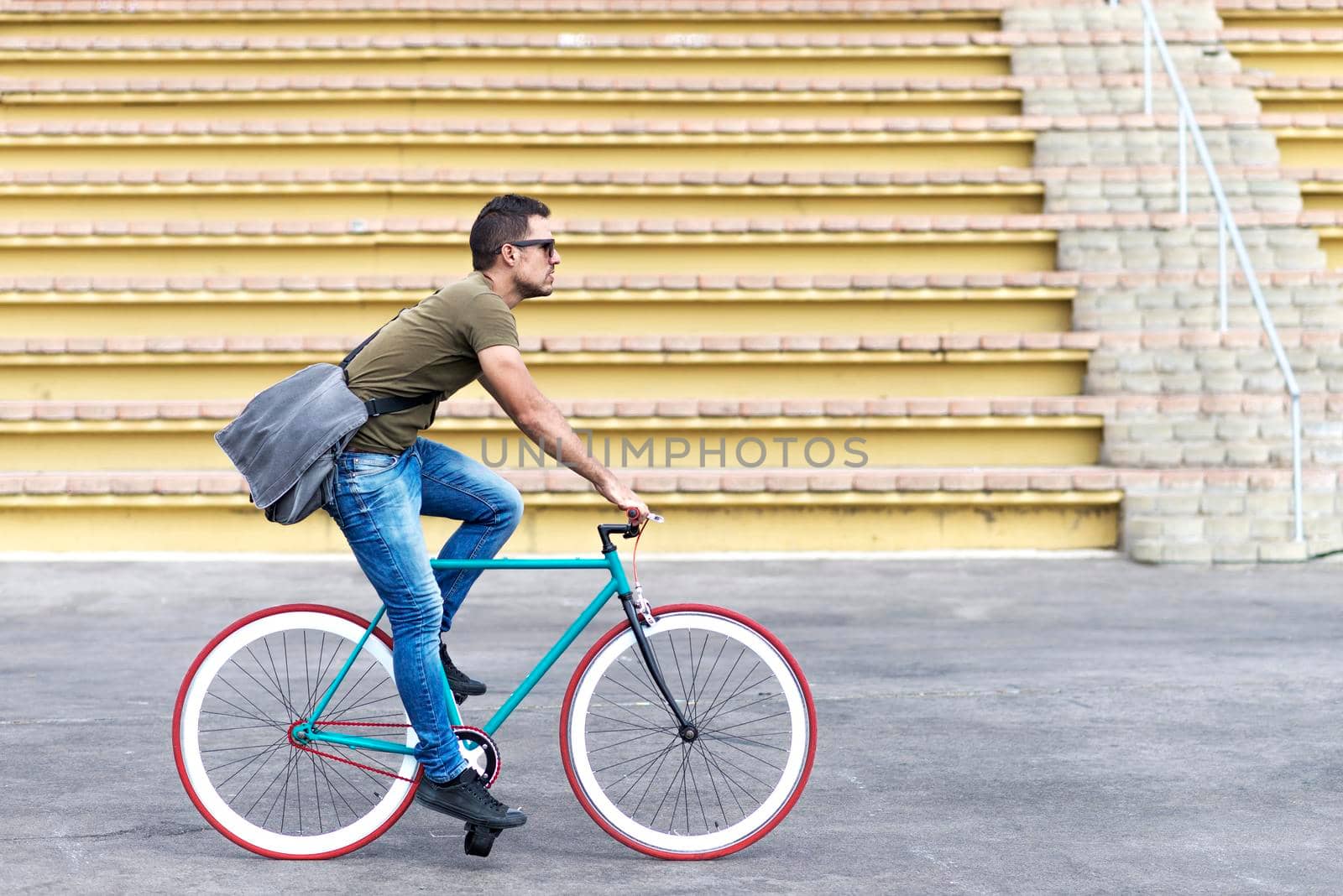 Man with sunglasses riding bicycle in urban city commuting trendy transportation by raferto1973
