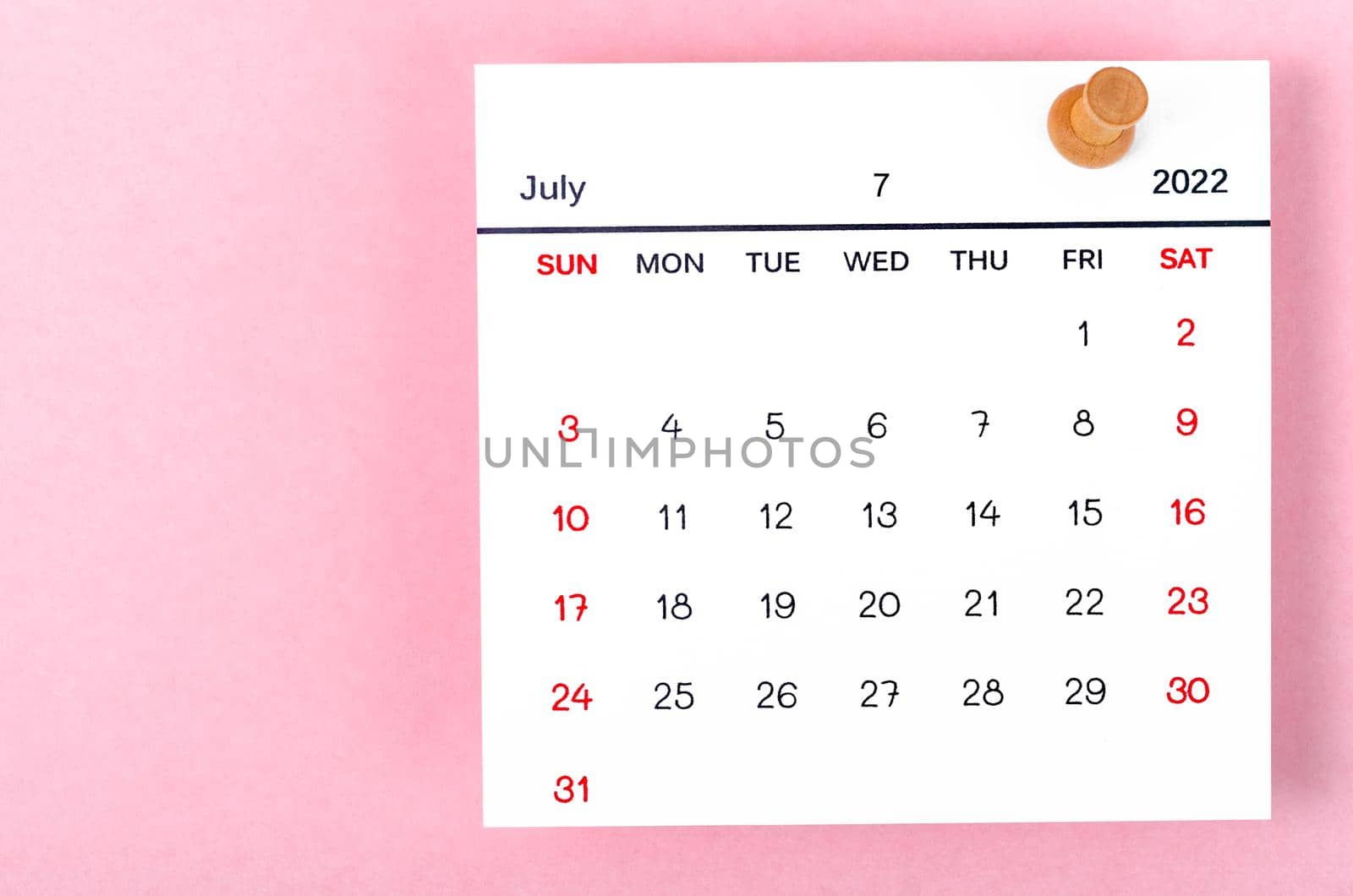 The July 2022 calencar and wooden push pin on pink background.