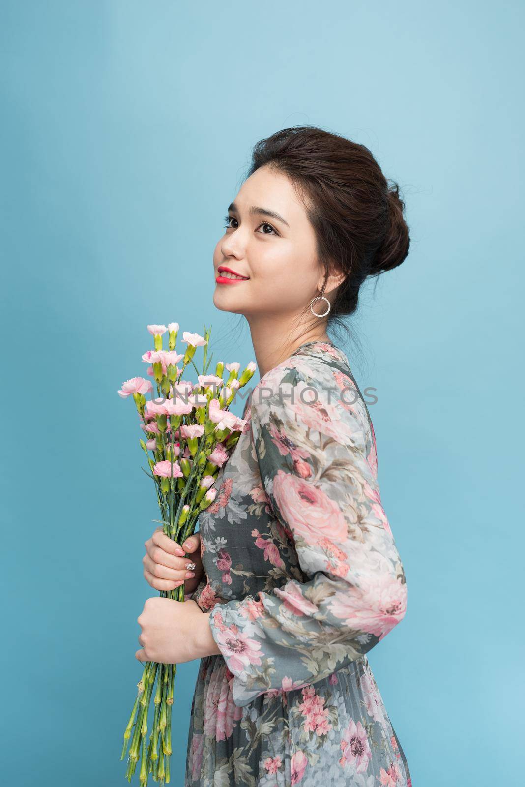 Attractive Asia woman in romantic dress holding bouquet of flowers over blue background