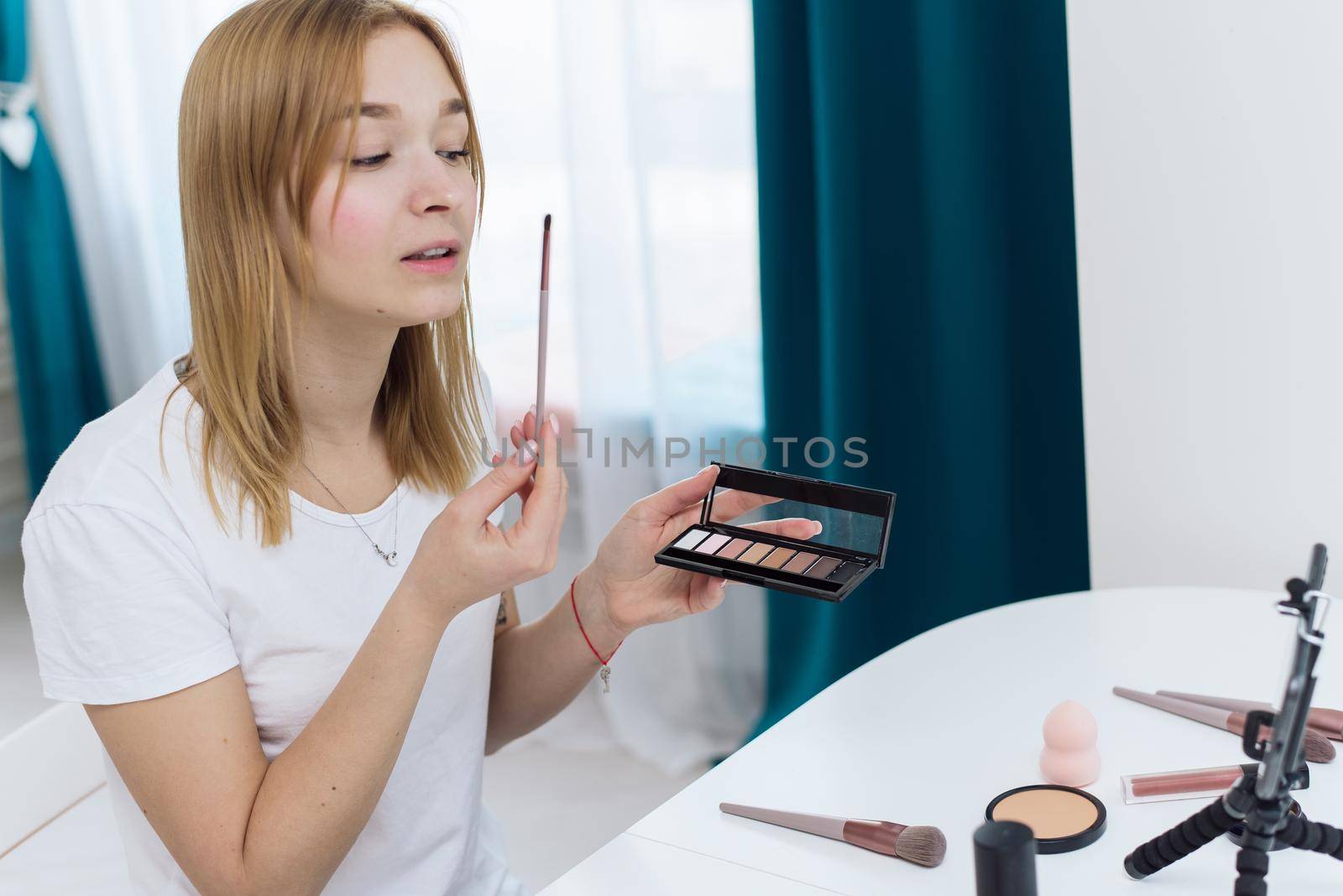 Beauty webinars, makeup classes online. Happy woman vlogger is showing cosmetics products while recording video stream on phone for her internet channel in social media. beauty blog about cosmetics and makeup.