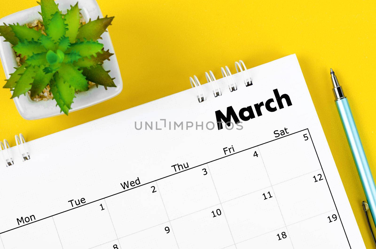 The March 2022 desk calendar and pen with plant pot on yellow background.