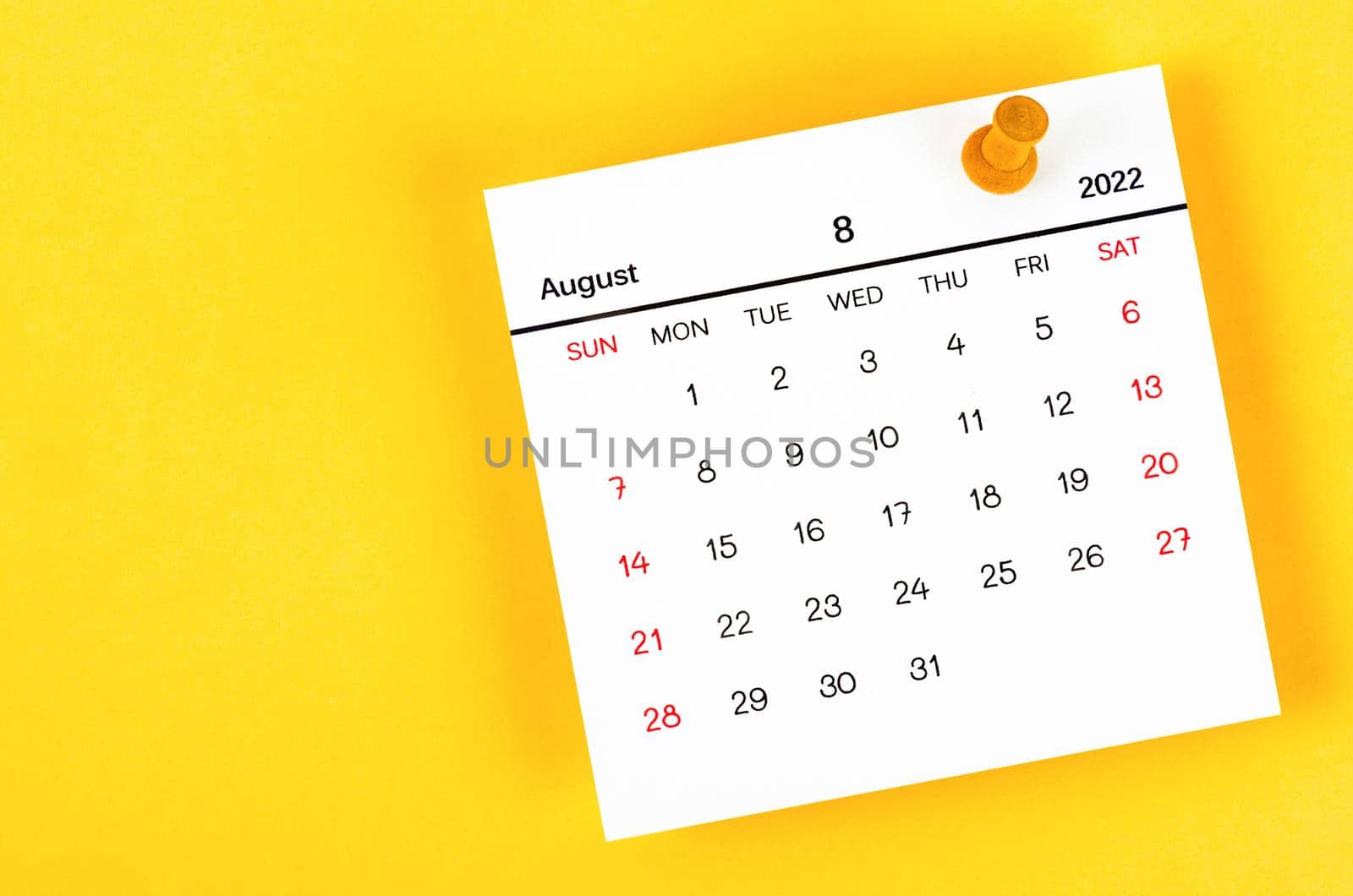 The August 2022 and wooden push pin on yellow background.