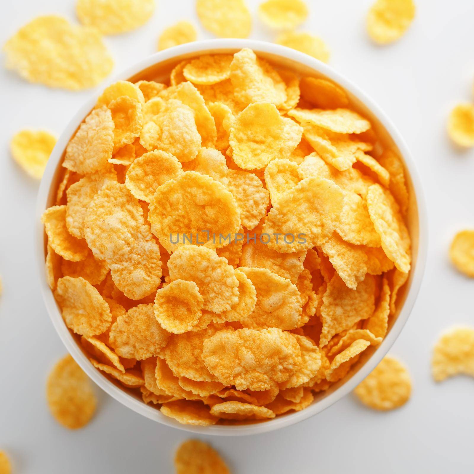White cup with golden corn flakes, isolated on white background. Hopya crumbled around the cup. View from above. Delicious and healthy breakfast