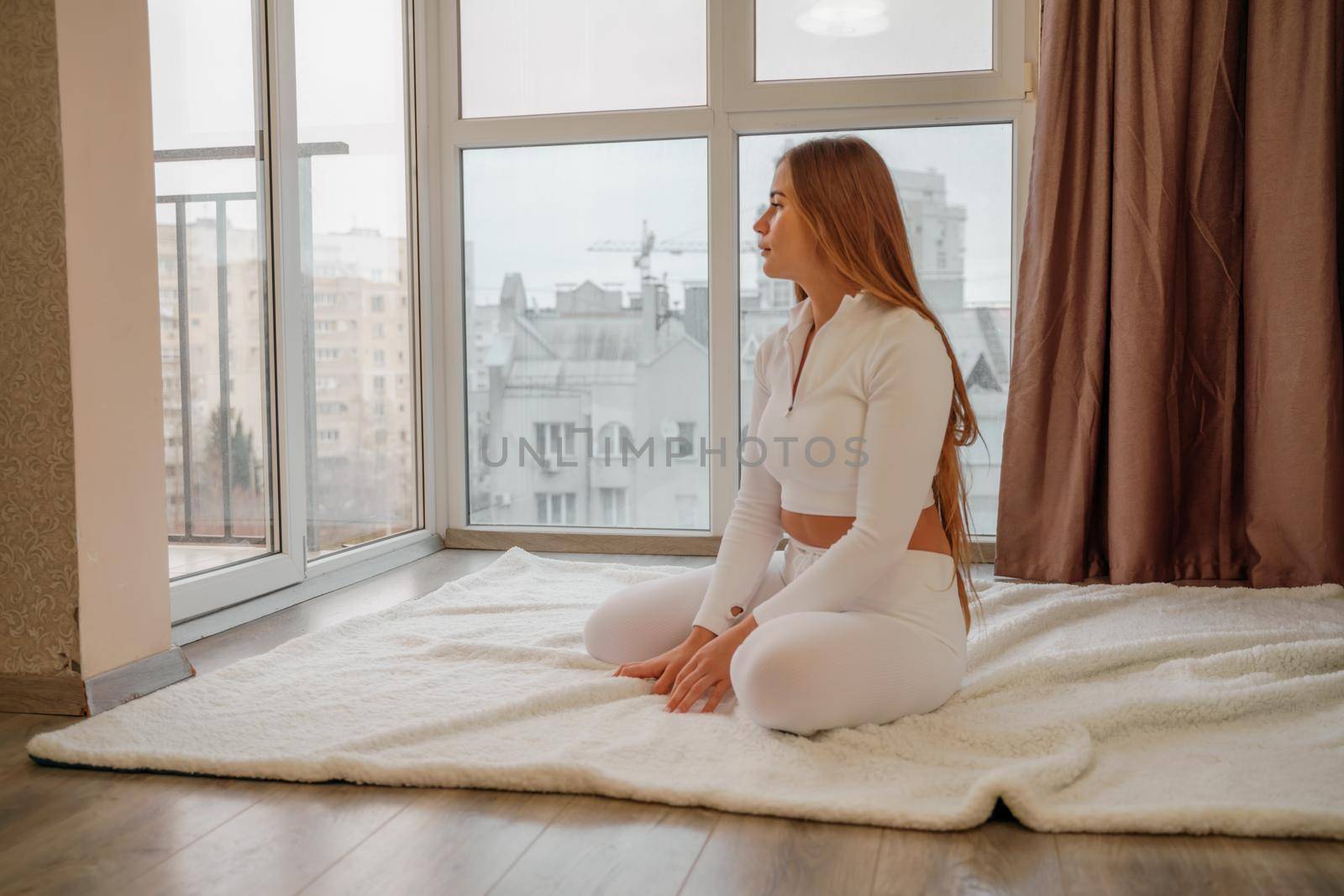 Side view portrait of relaxed woman listening to music with headphones lying on carpet at home. She is dressed in a white tracksuit