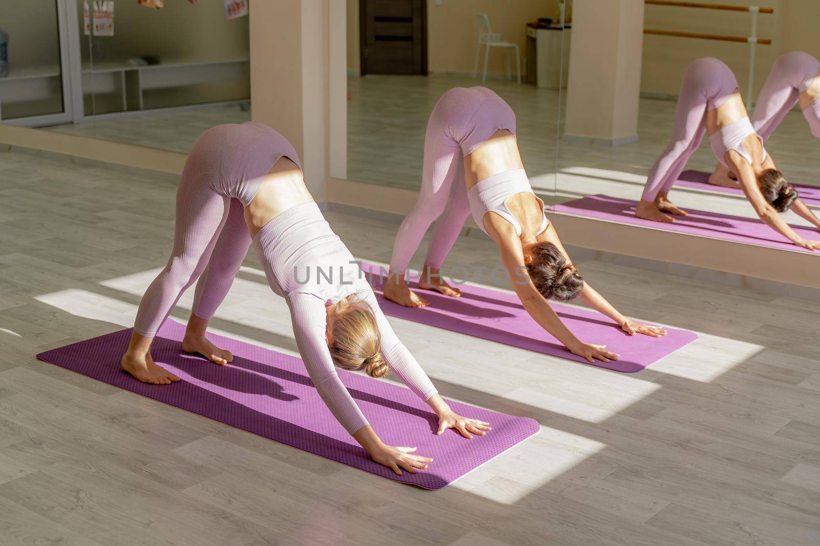 Two beautiful women cook doing yoga, sports together in the gym. Dressed in pink suits. The concept of grace and beauty of the body