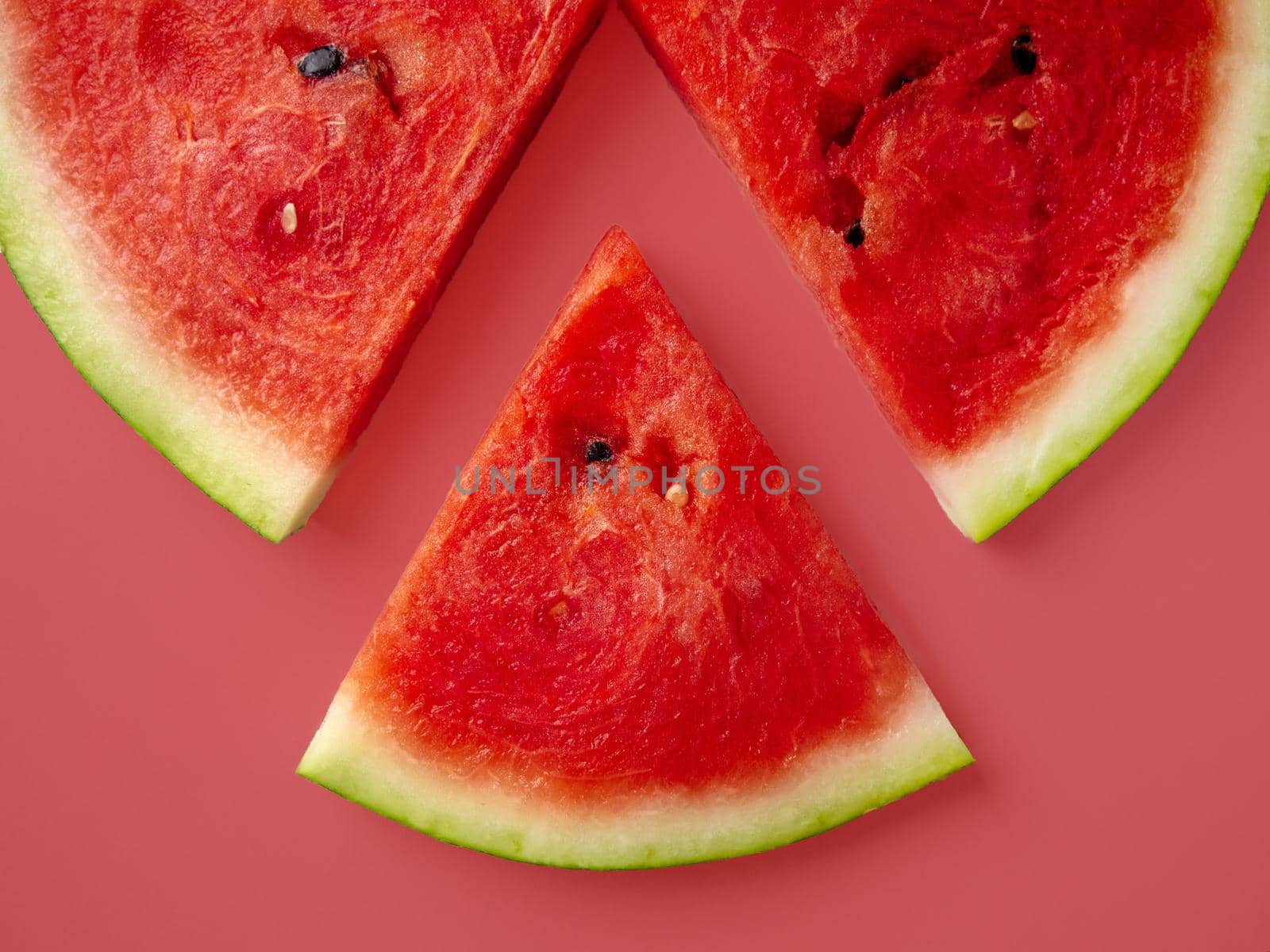 Slices of fresh red delicious watermelon are laid out in a circle on a colored background.