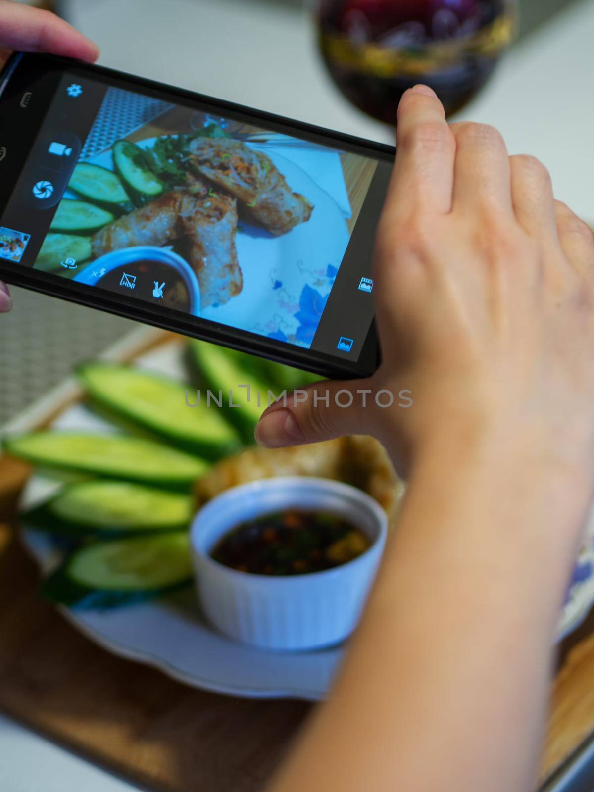 Hand using a smartphone to photograph fried Vietnamese pancakes - nem, with vegetables