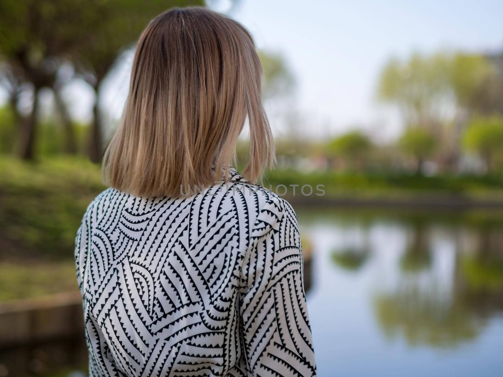 stylish blonde woman in a black and white cloak by the lake in the park