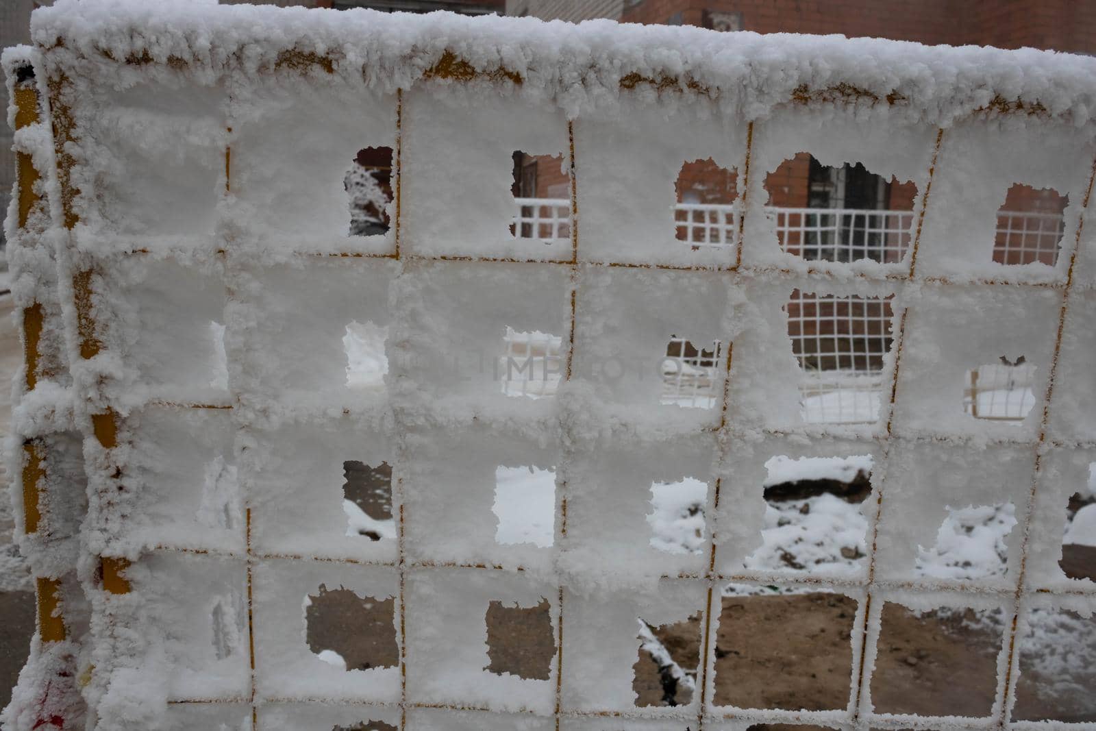 The fence grid is strewn with frost crystals, snowflakes. Winter snowy frosty background. World Snow Day.