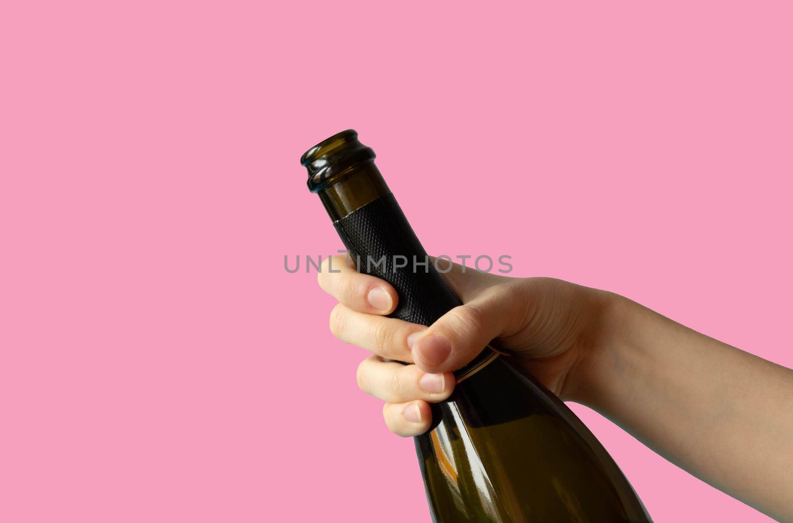 A woman's hand holding an open bottle of champagne on a pink background.