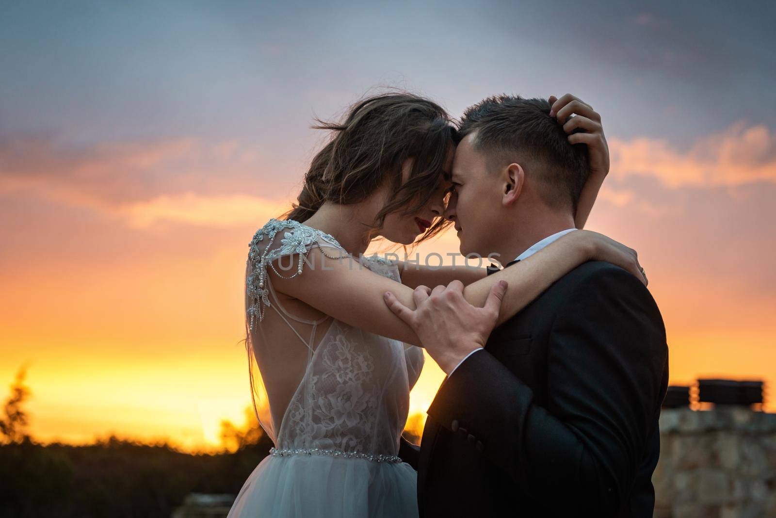 Bride and Groom close-up sensually lean their faces against each other in the sunlight. The dreamy bride gently embraces her groom with eyes closed in the sunlight. close-up The bride and groom are embracing on a beautiful old street. by Andrii_Ko