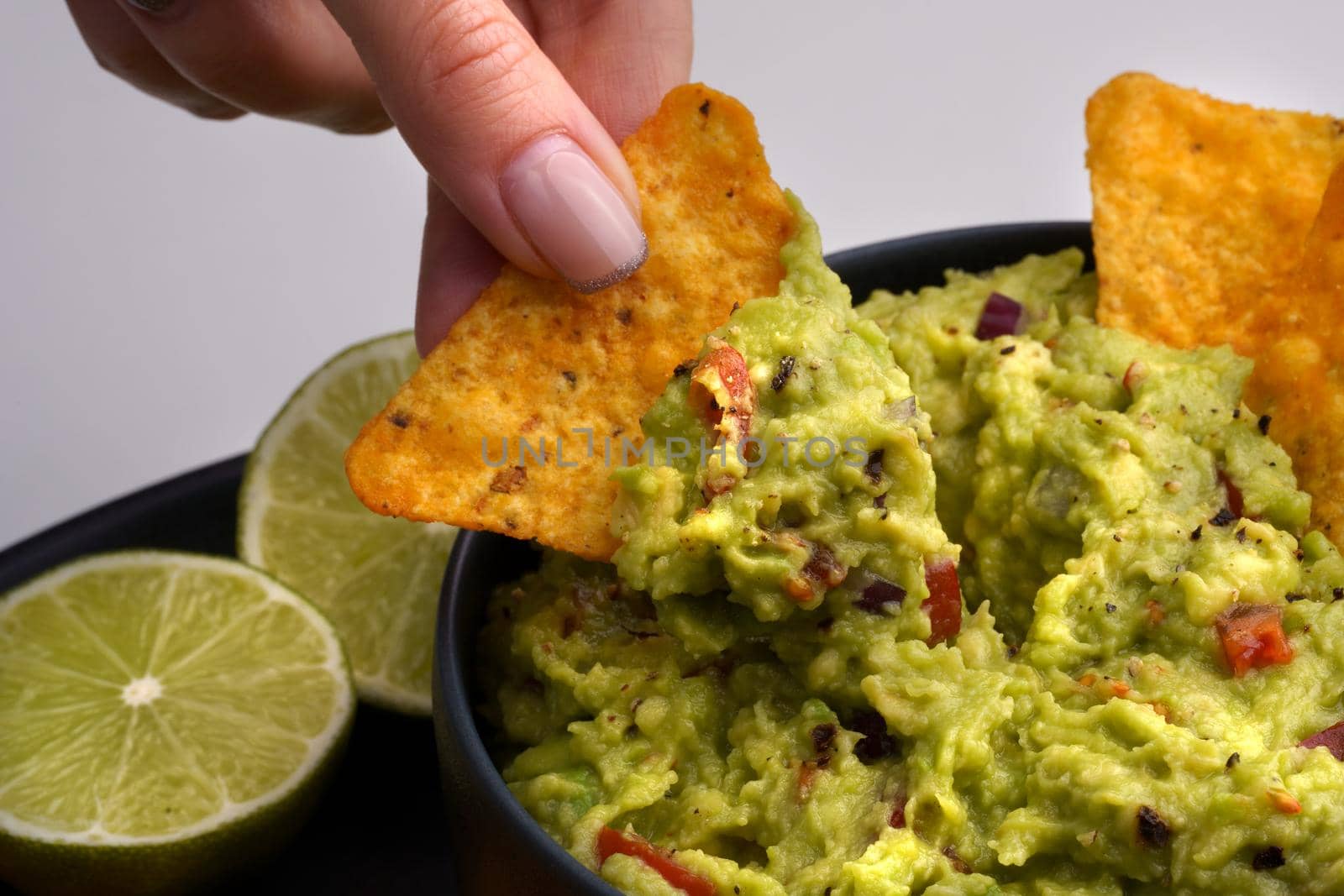 Closeup of woman hand with tortilla chip or nachos with tasty guacamole dip. High quality photo