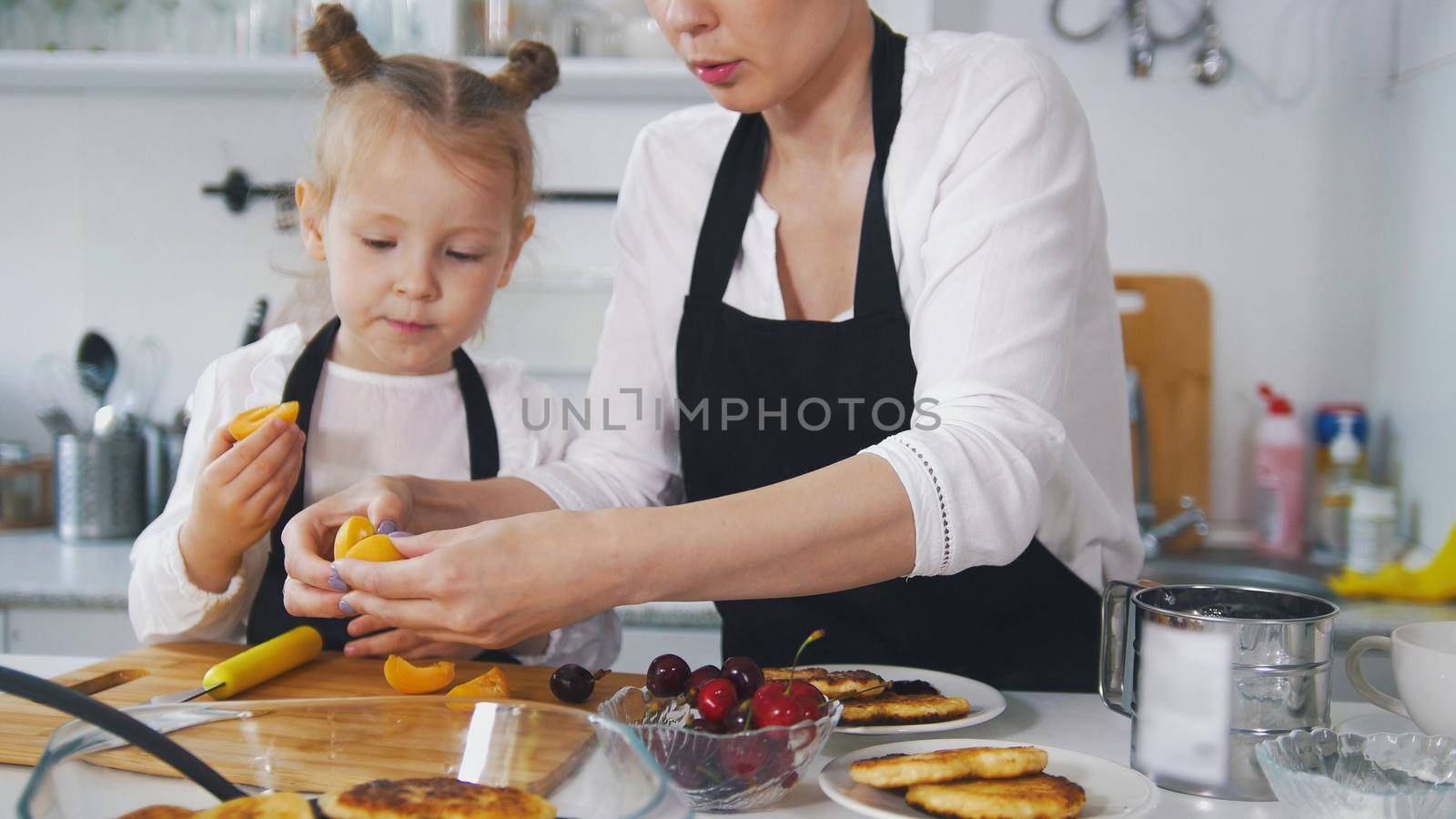 Little girl talking with her mother which cooking cottage cheese pancakes in the kitchen by Studia72