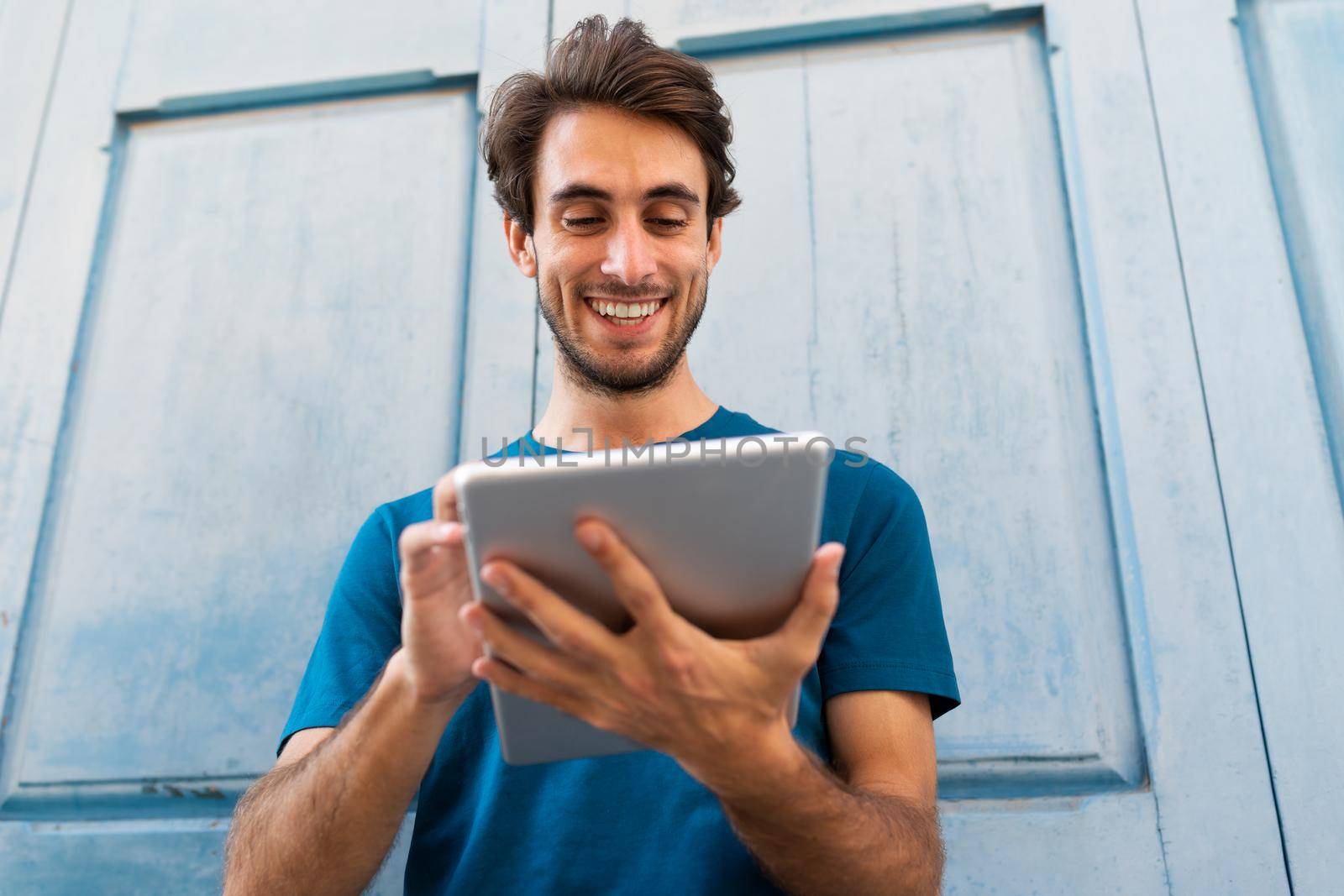 Happy smiling young caucasian man using digital tablet outdoors. Wireless technology and social media concept.