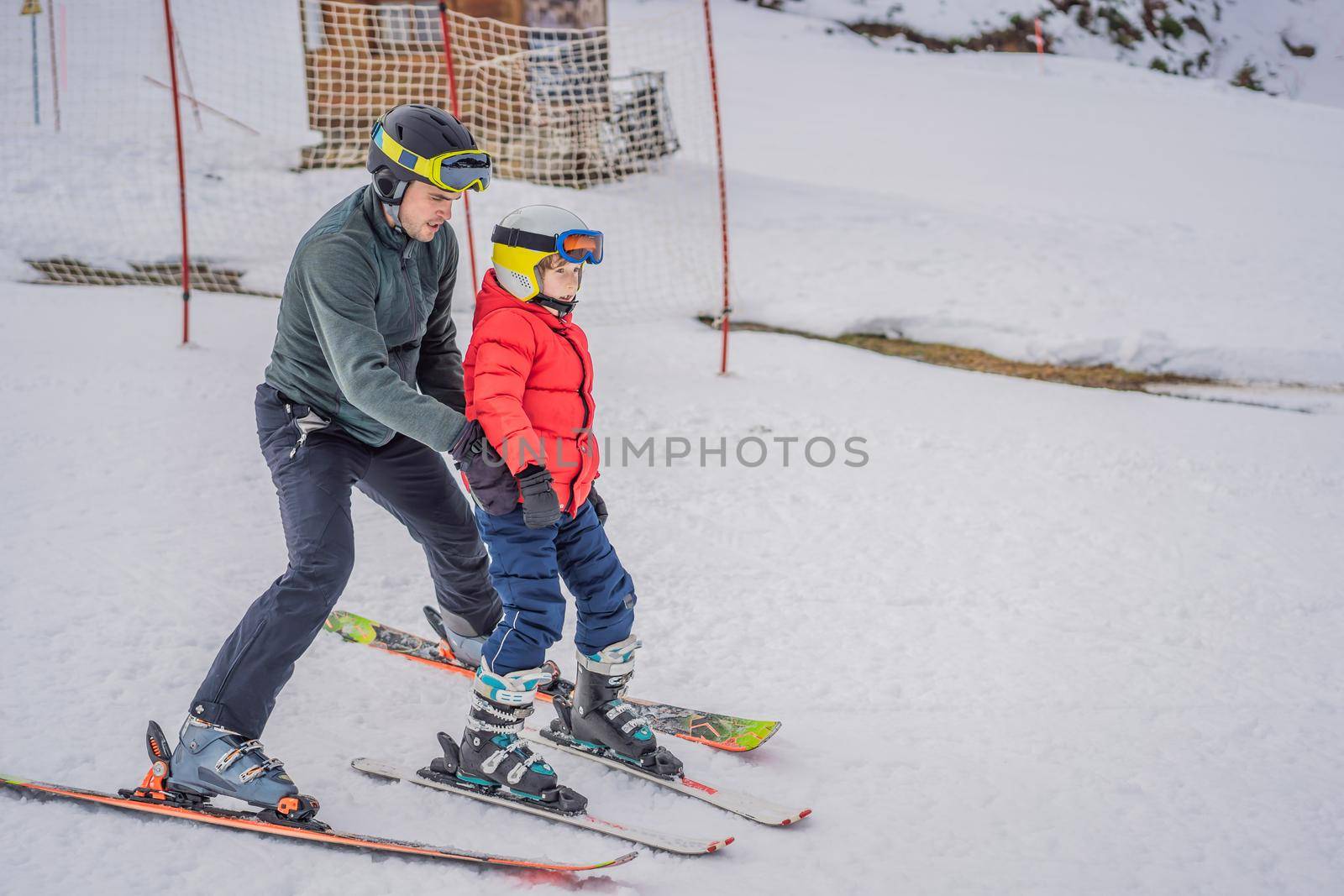 Boy learning to ski, training and listening to his ski instructor on the slope in winter.