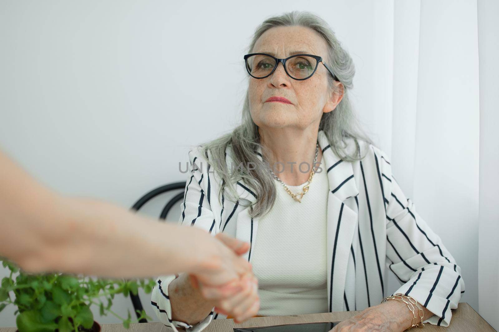 Mature businesswoman is leading an interview with new colleague and shaking their hand at the end. Business people concept.