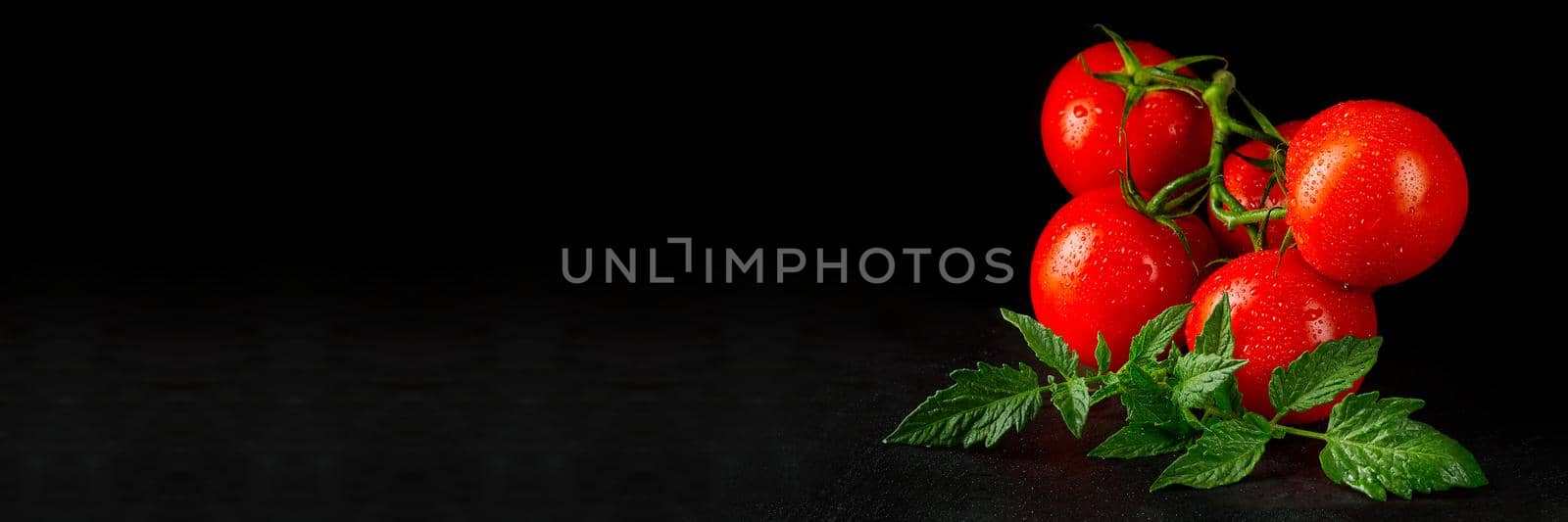 Ripe organic tomatoes on the black table in low key with water drops by PhotoTime