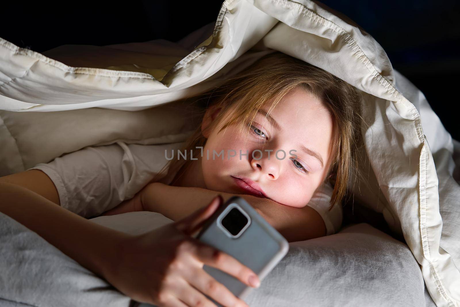 Portrait of girl with mobile phone under blanket at night. Gadget night. Social media addiction. Cyber bullying by PhotoTime