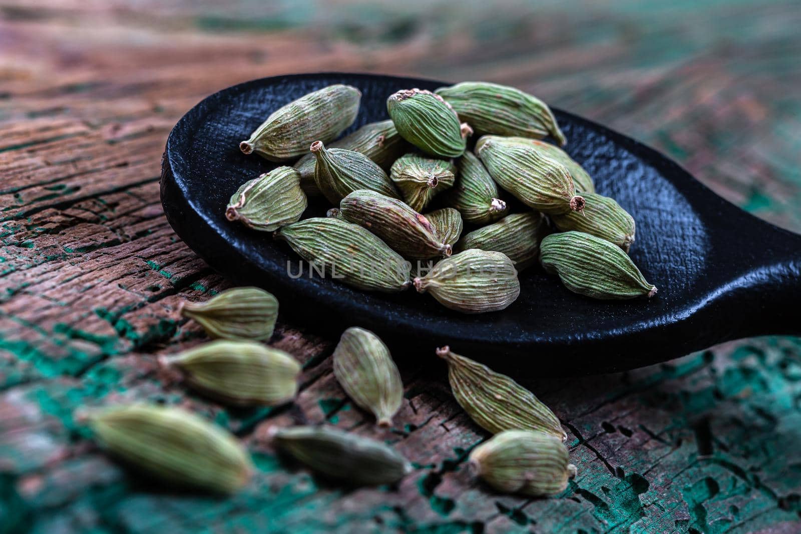 Macro cardamom seeds in a black wooden spoon