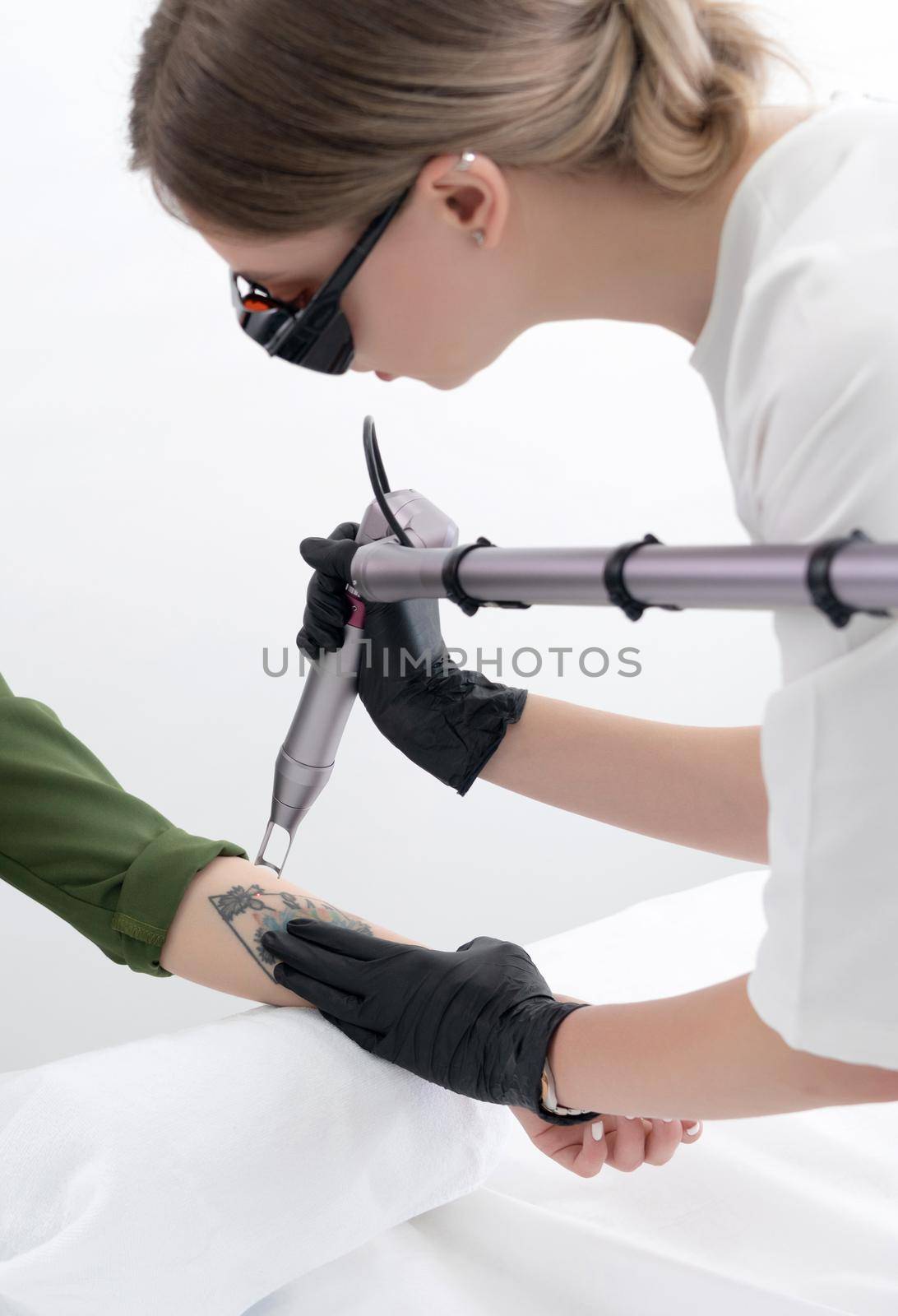 Beautician using laser device to remove an unwanted tattoo from female arm. Concept of erasing tattoos as an expensive procedure in a cosmetology clinic by Mariakray