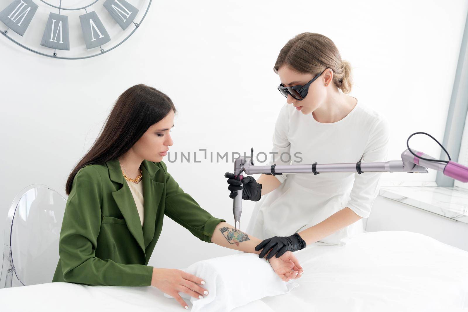 Beautician using laser device to remove an unwanted tattoo from female arm. Concept of erasing tattoos as expensive procedure in a cosmetology clinic