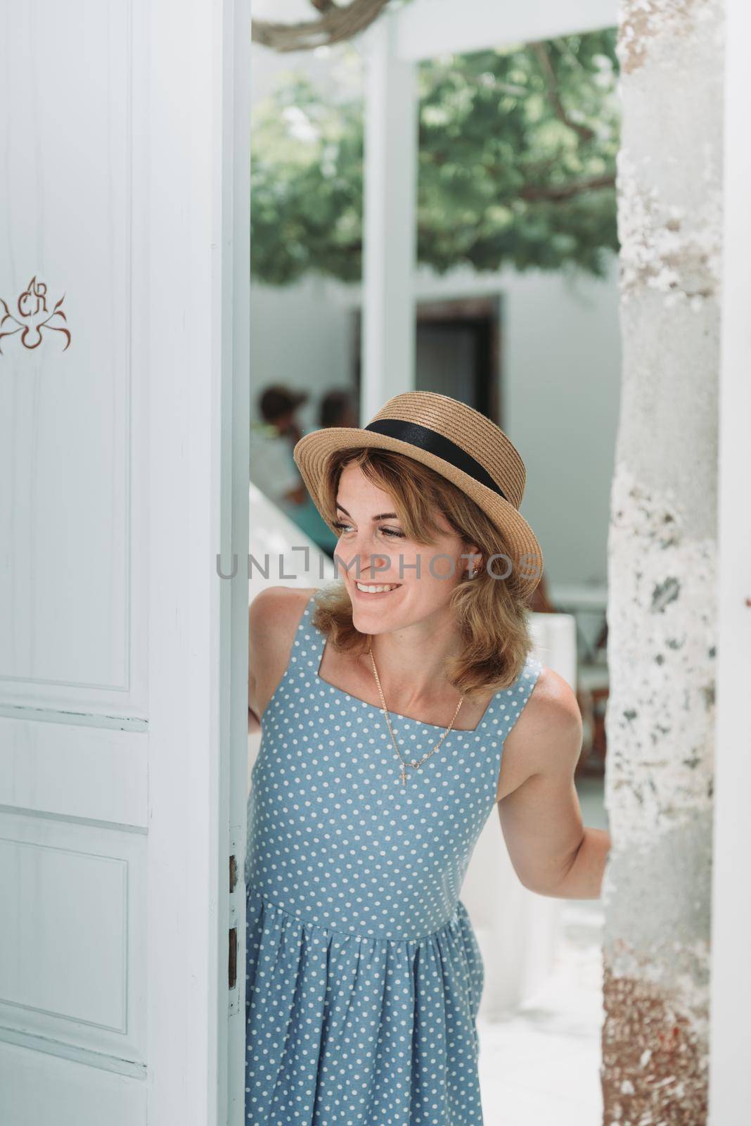 Travel Europe for summer holiday. Portrait of beautiful woman visitting old village Oia, Santorini island, Greece with sun hat and summer dress. by Andrii_Ko