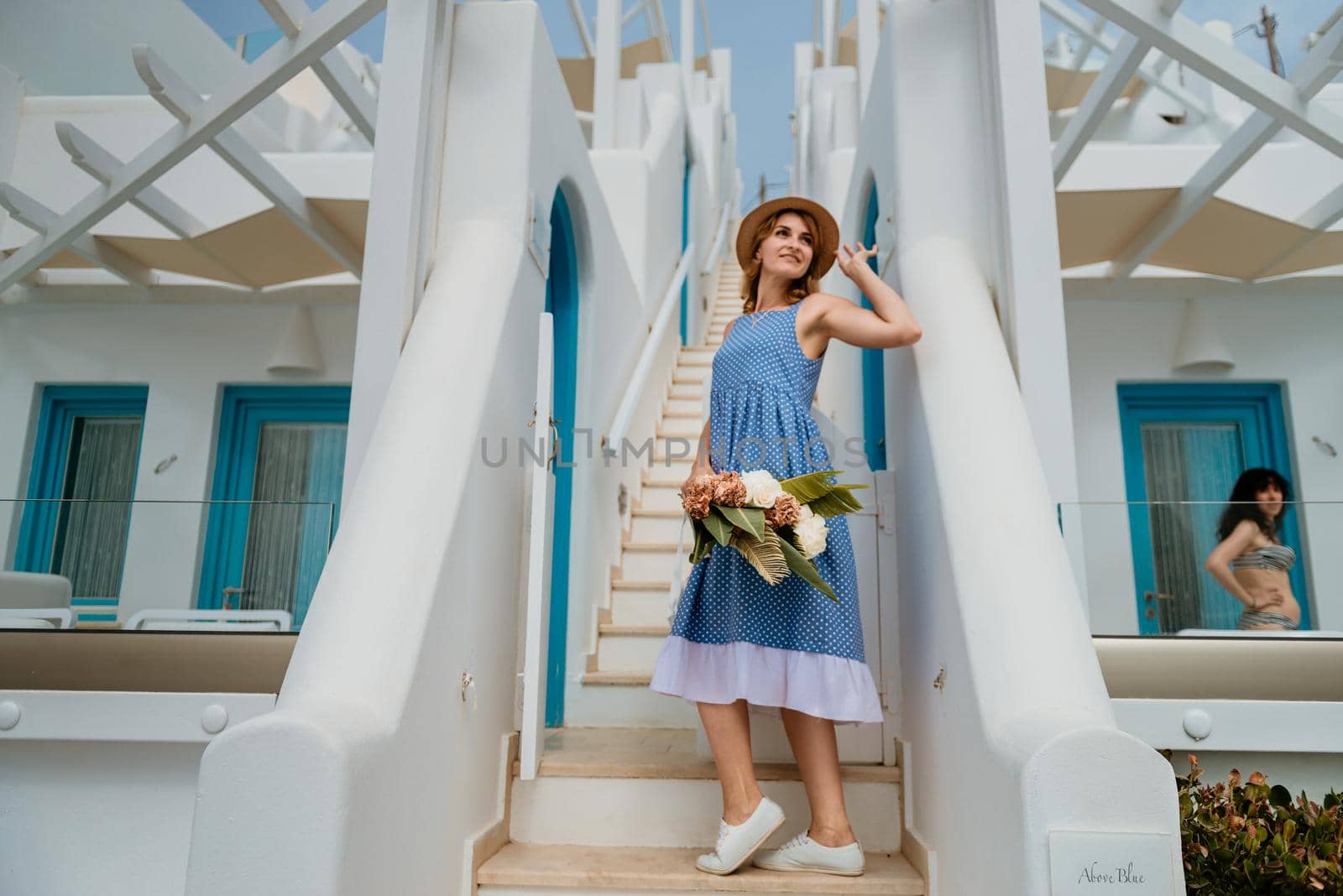 Beautiful girl walking with bouquet of flowers along the street of Santorini island, an old European town, Greece. Portrait of a tourist girl walking on the street background. Love story summer vacation by Andrii_Ko