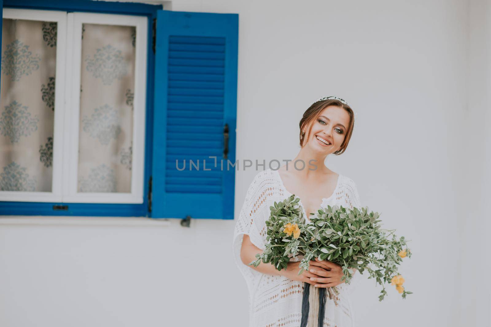 Beautiful bride on a background of white architecture with blue window on Santorini island, Greece,a popular wedding destination by Andrii_Ko