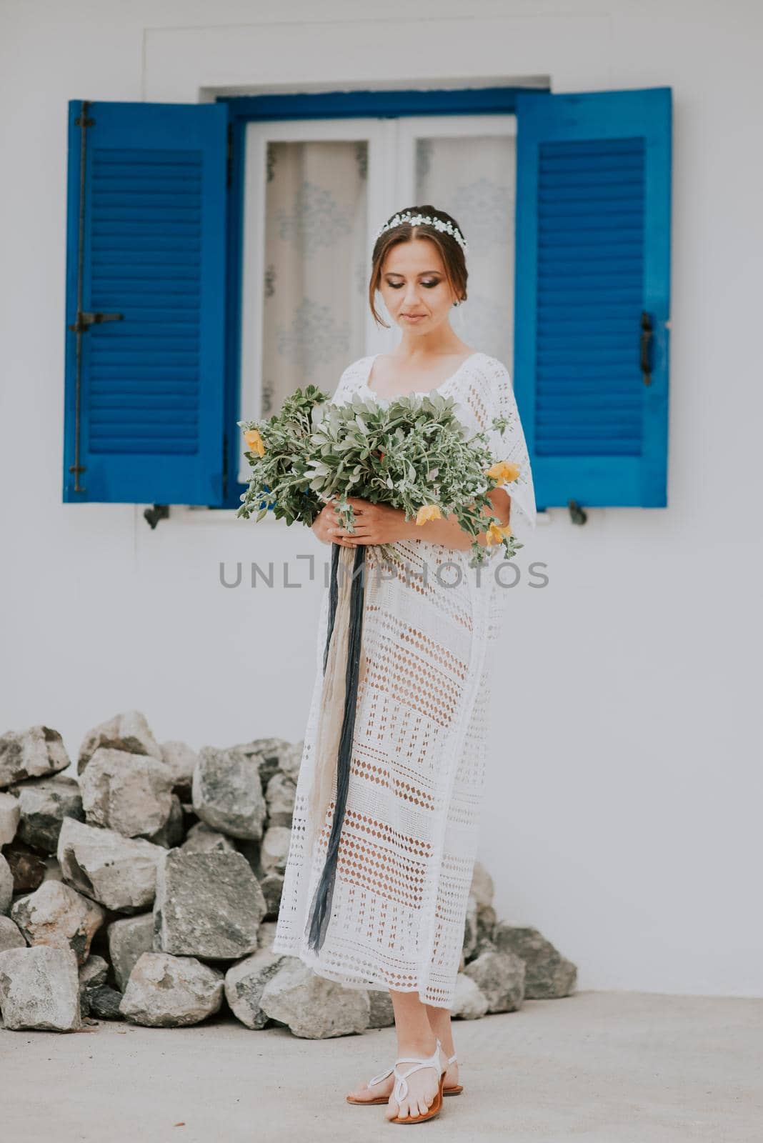 Handsome beautiful caucasian bride posing near white wall with blue windows. Young attractive bride with the bouquet of flowers by Andrii_Ko