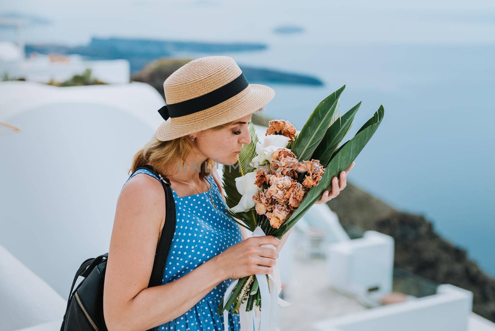 Beautiful girl walking with bouquet of flowers along the street of Santorini island, an old European town, Greece. Portrait of a tourist girl walking on the street background. Love story summer vacation by Andrii_Ko