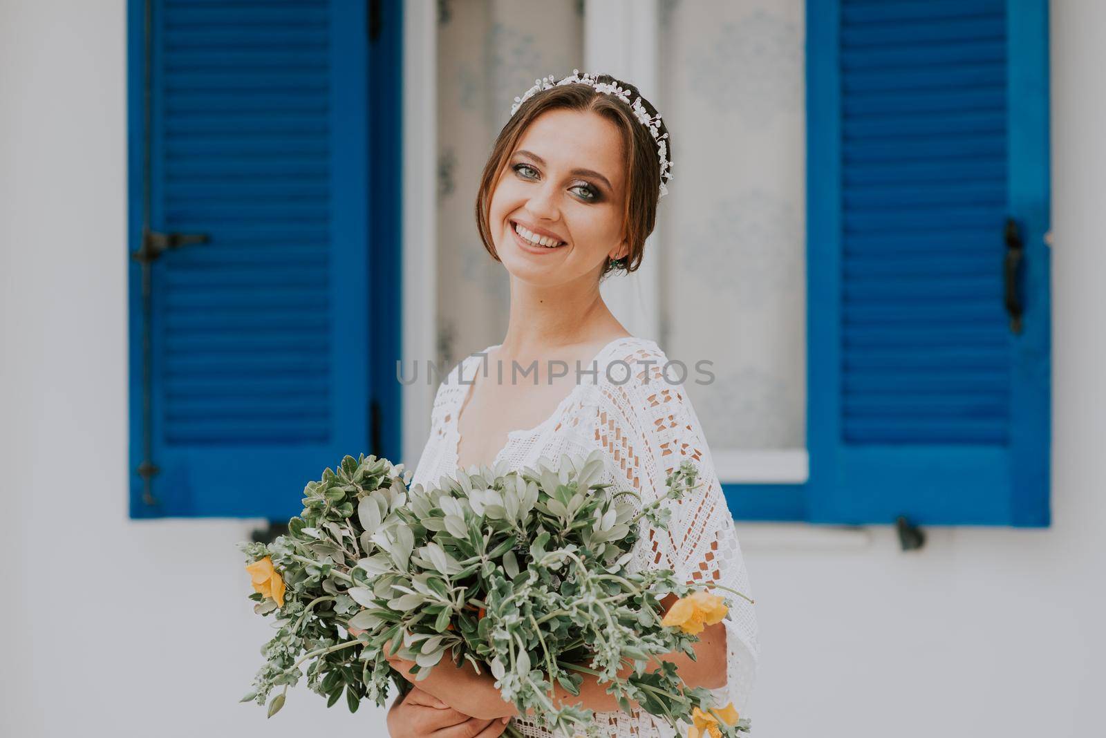 Handsome beautiful caucasian bride posing near white wall with blue windows. Young attractive bride with the bouquet of flowers by Andrii_Ko