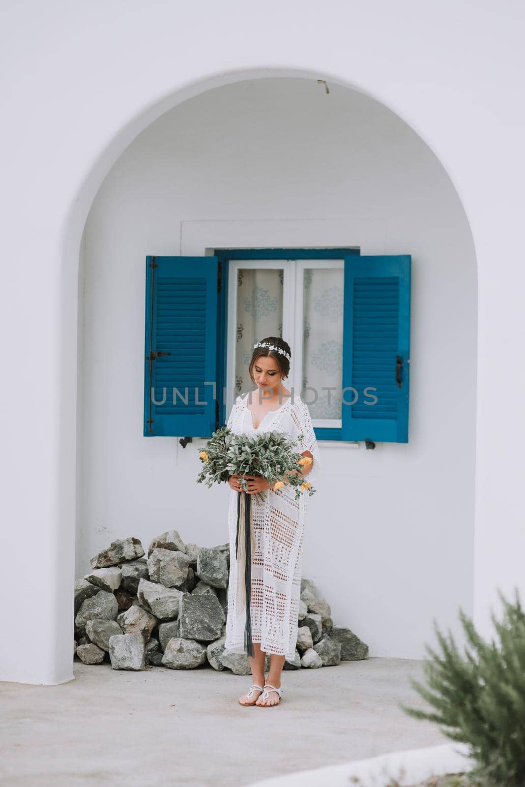 Handsome beautiful caucasian bride posing near white wall with blue windows. Young attractive bride with the bouquet of flowers by Andrii_Ko