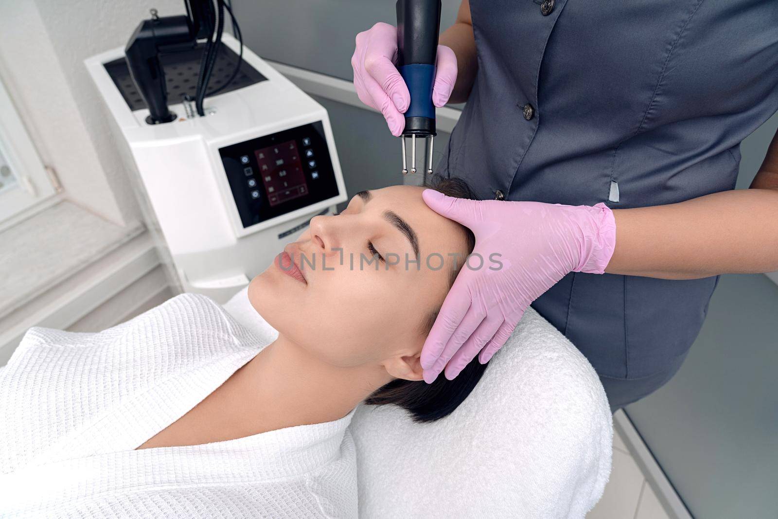 Cosmetology. Beautiful Woman At Spa Clinic Receiving Stimulating Electric Facial Treatment From Therapist. Closeup Of Young Female Face