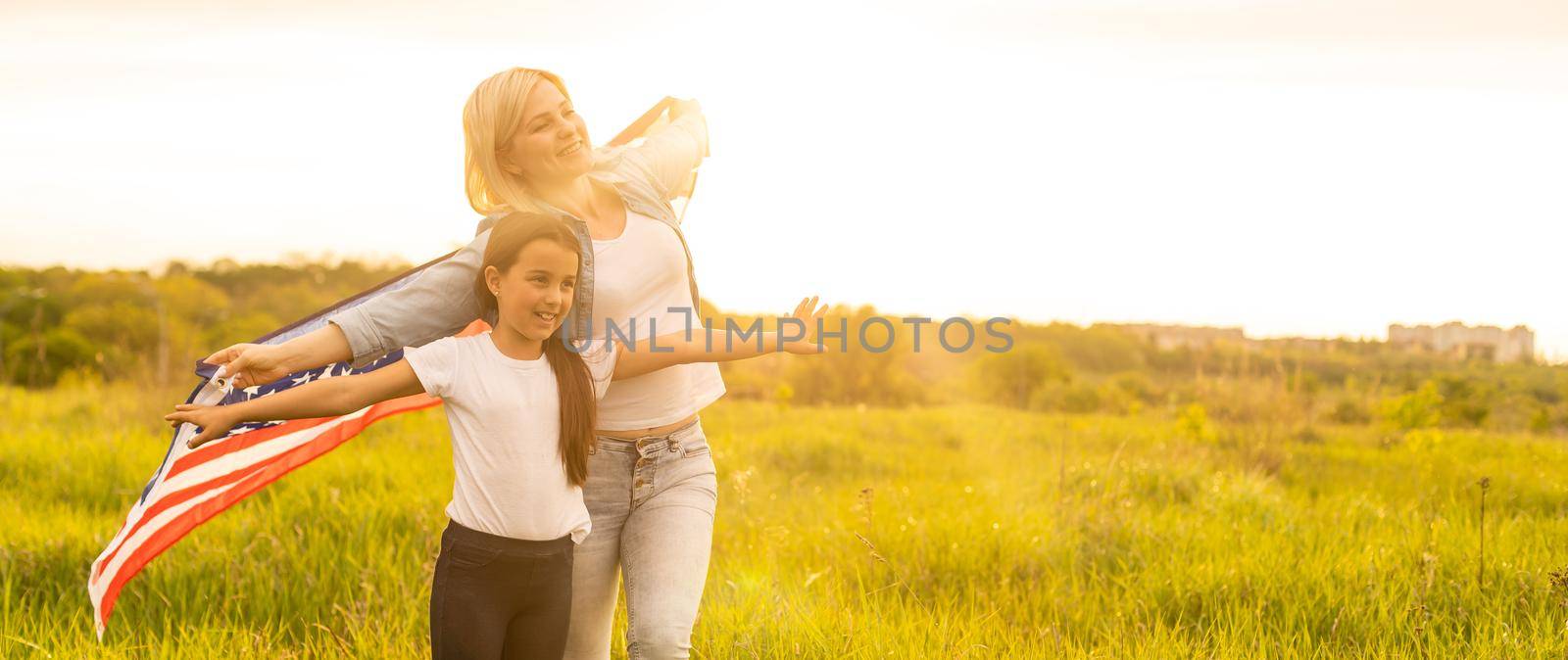 Patriotic holiday. Happy family, mother and her daughter child girl with American flag outdoors. USA celebrate 4th of July.