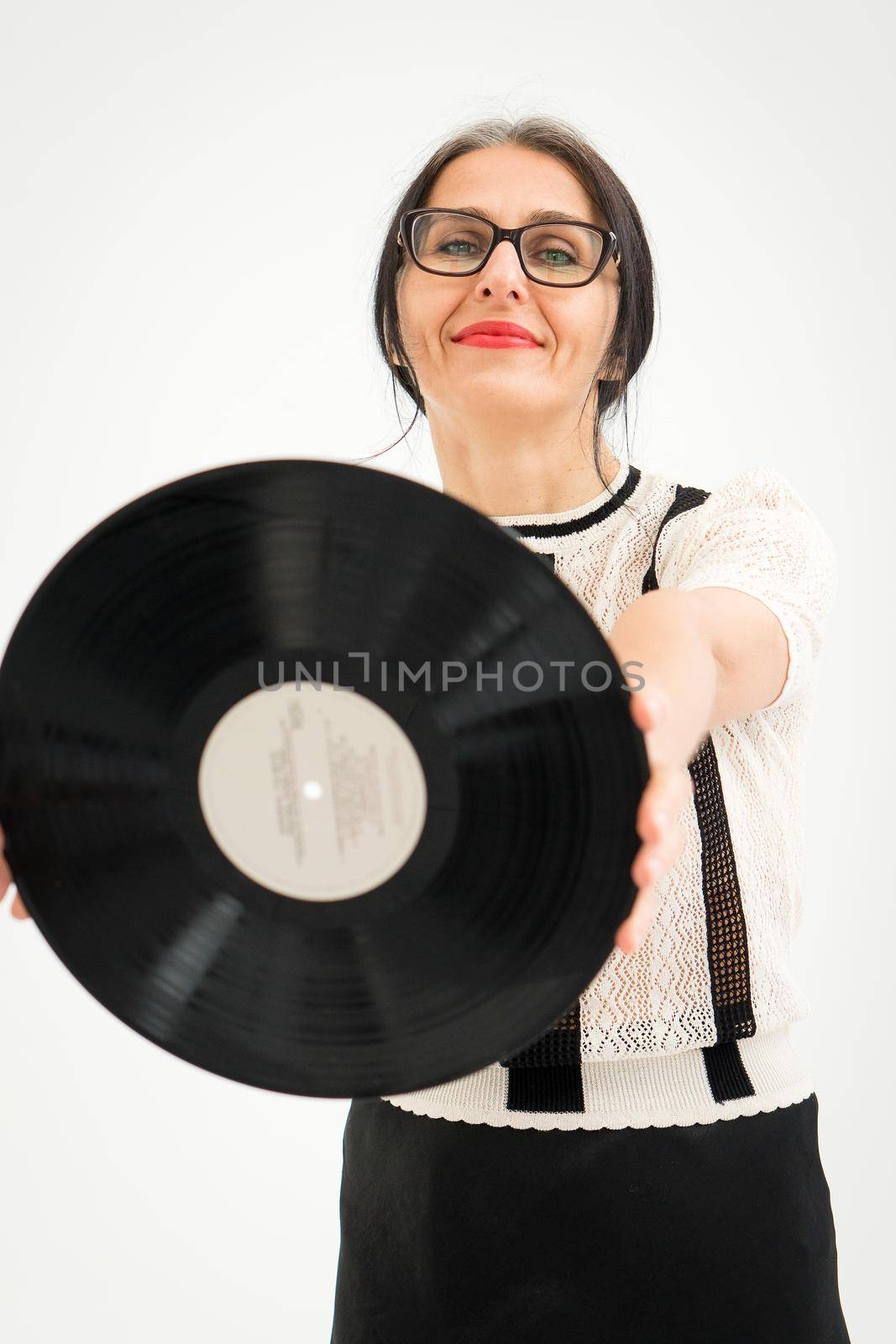 Studio photo of middle aged woman starting getting grey-haired wearing black and white clothes with vinyl record in hands on white background, middle age sexy lady, happy life concept by balinska_lv
