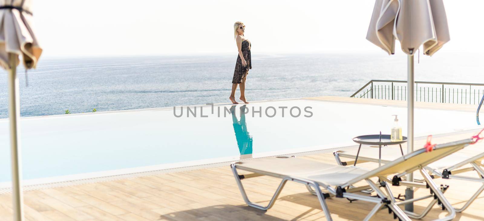 An attractive young woman stands near the pool with a panoramic view.