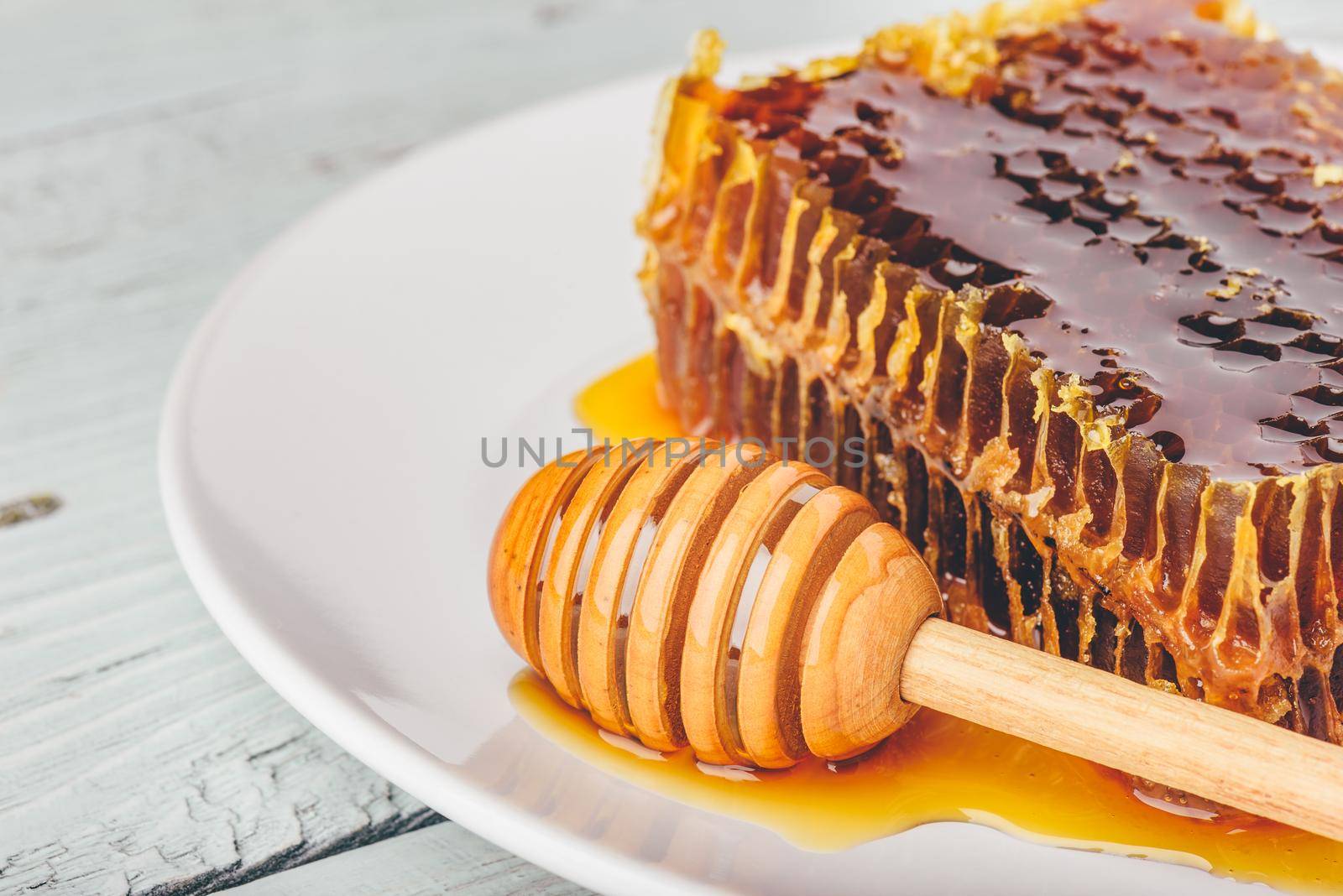 Delicious honeycomb on white plate with wooden honey dipper