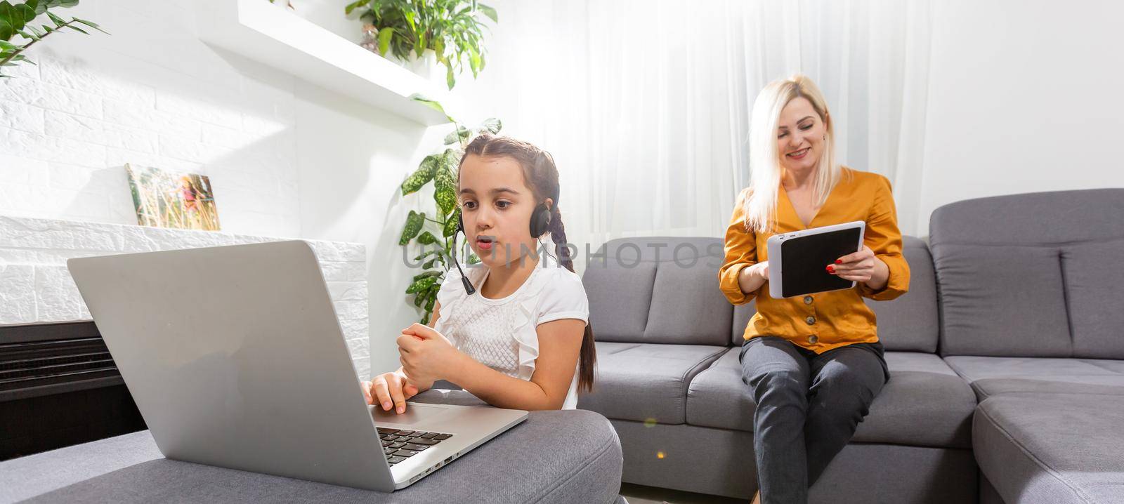 smiling young mother and daughter studying online classes in home office in the modern living room by Andelov13