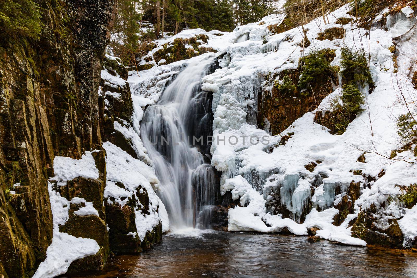 Long high waterfall in mountains full of snow and ice around