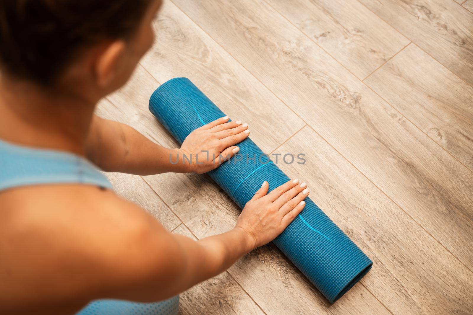 Woman hands rolled up yoga mat on gym floor in yoga fitness training room. Home workout woman close up hands rolling foam yoga gym mat. Woman barefoot home workout sportive healthy lifestyle concept.