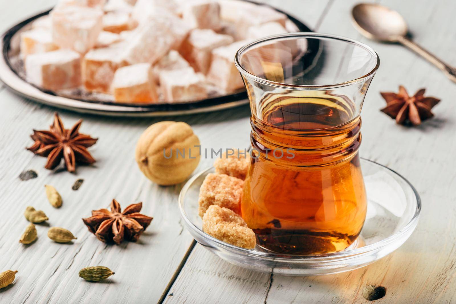Tea in arab glass with turkish delight Rahat Lokum and different spices over wooden surface