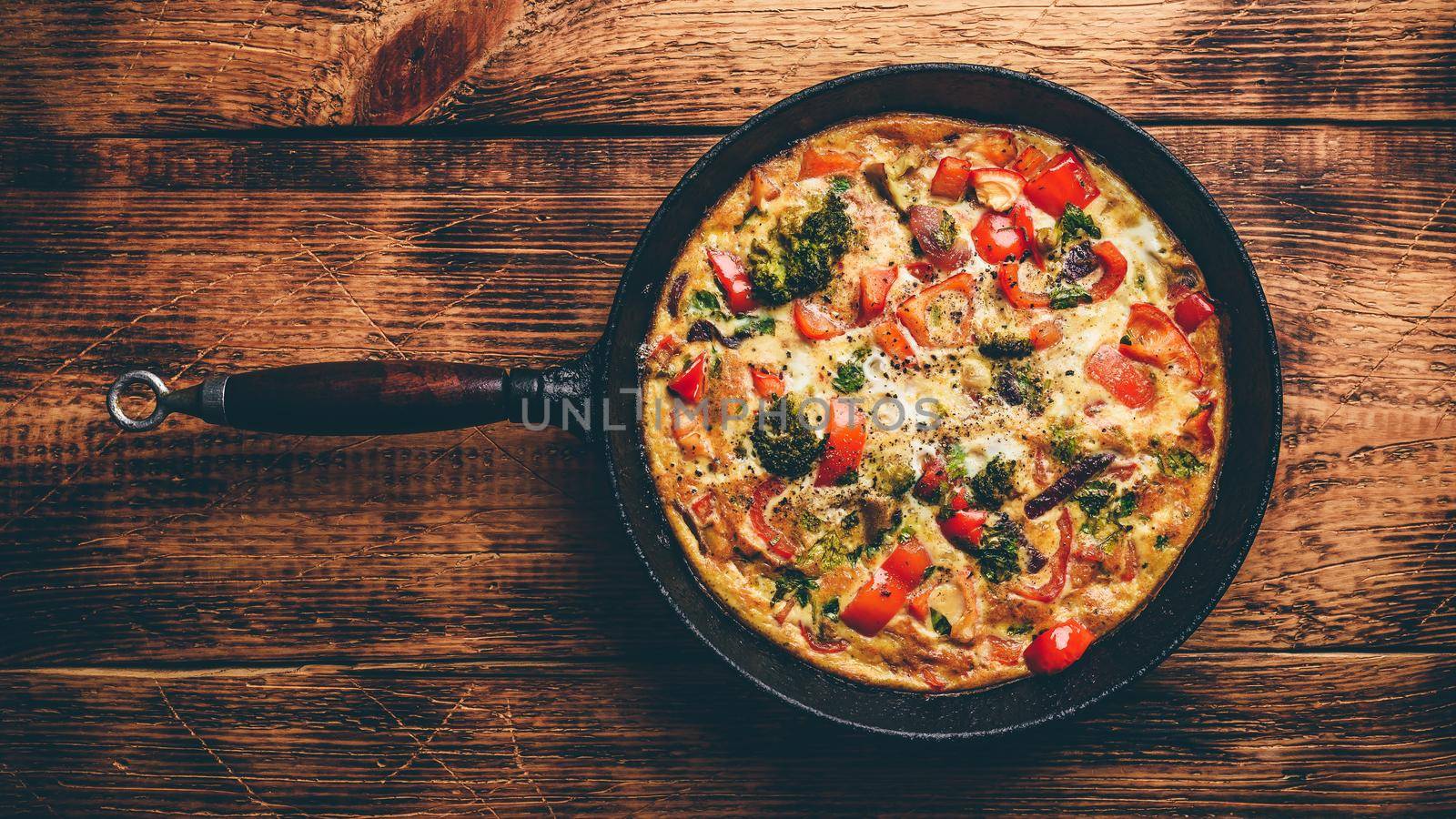 Vegetable frittata with broccoli, red bell pepper and red onion in cast iron skillet. View from above