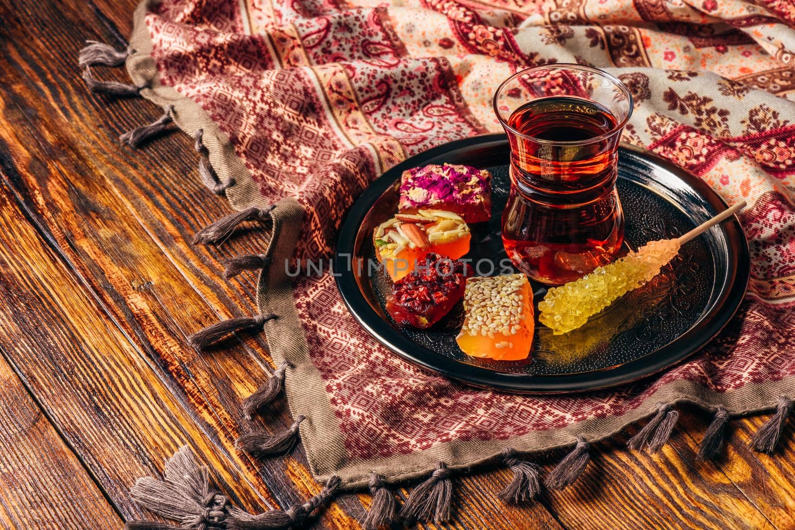 Tea in armudu glass with oriental delight rahat lokum on metal tray over wooden surface and tablecloth