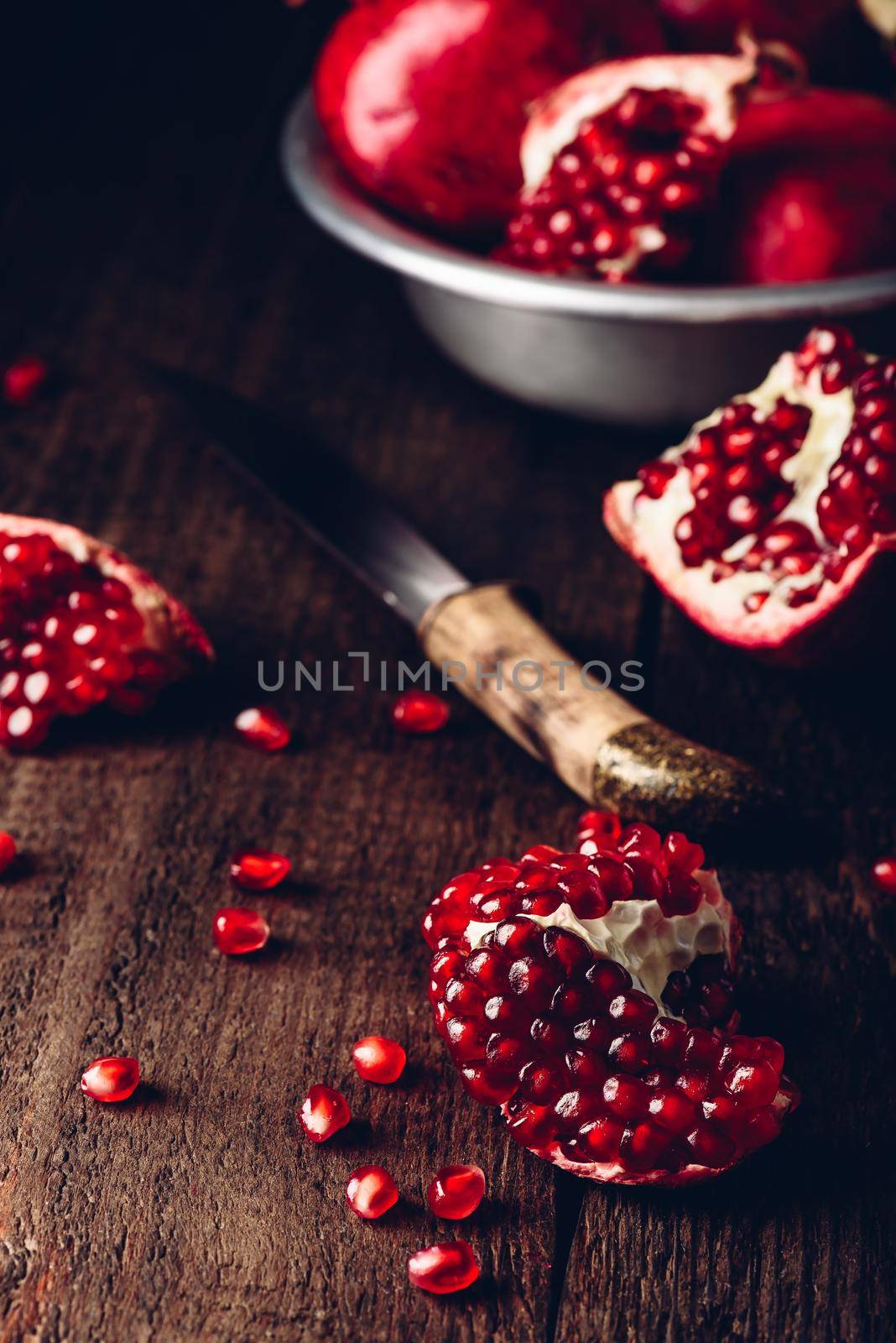 Pomegranate pieces with knife on rustic wooden surface.